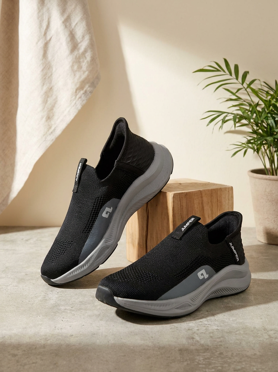 Black and gray slip-on shoes on a light wooden surface with a plant in the background