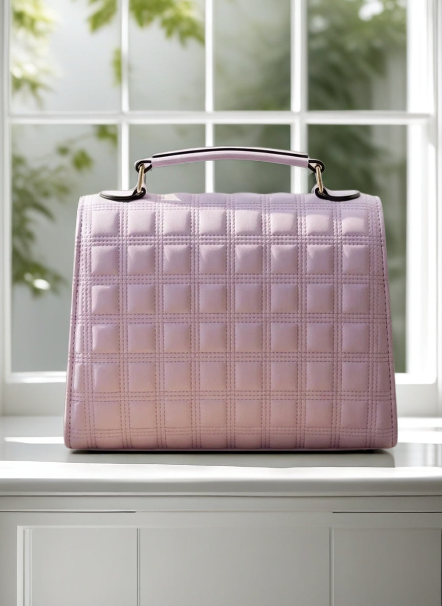 Pink quilted handbag on a white surface with a blurred green background