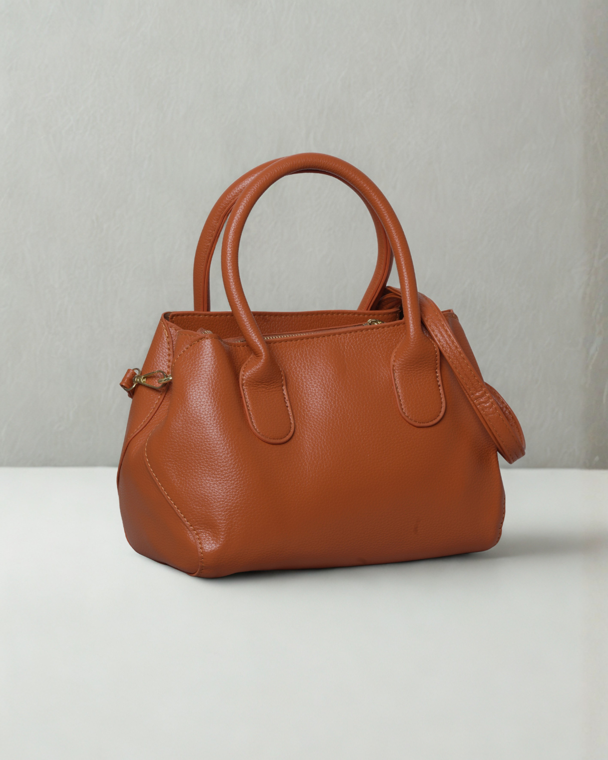 Brown leather handbag on a white surface with a light gray background