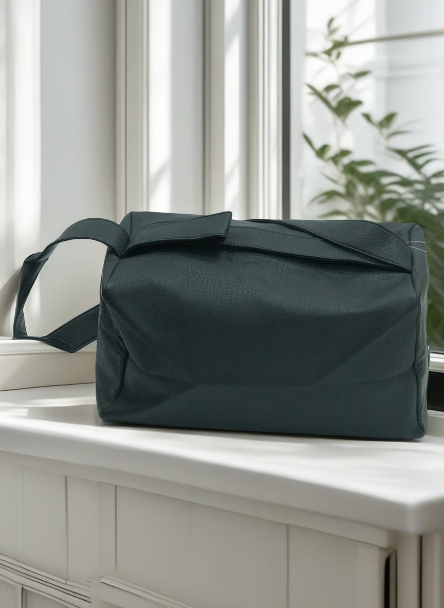 Dark green bag on a white surface with a window and plant in the background