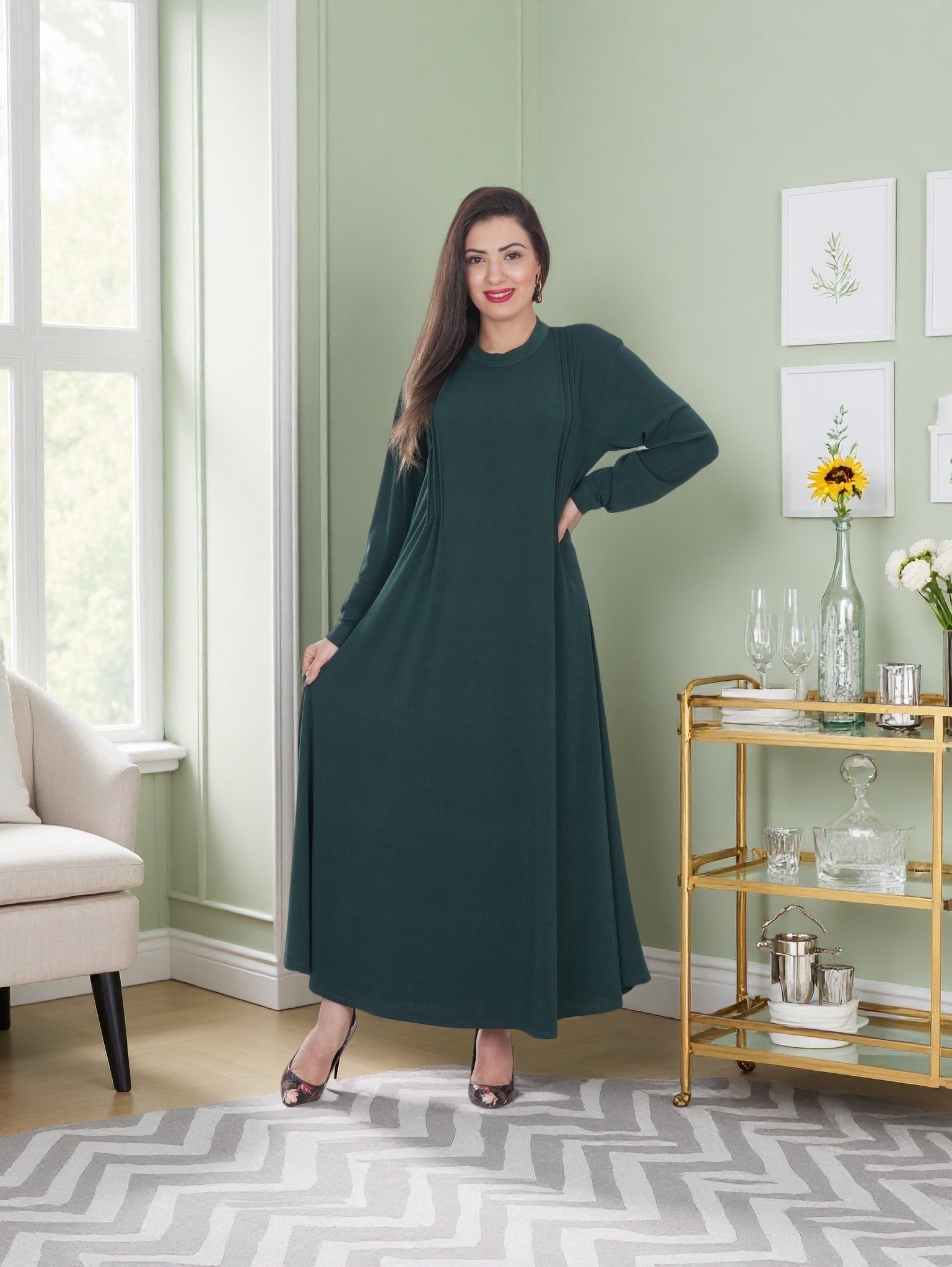 Woman in a green dress standing in a room with a gold bar cart and decorative items.