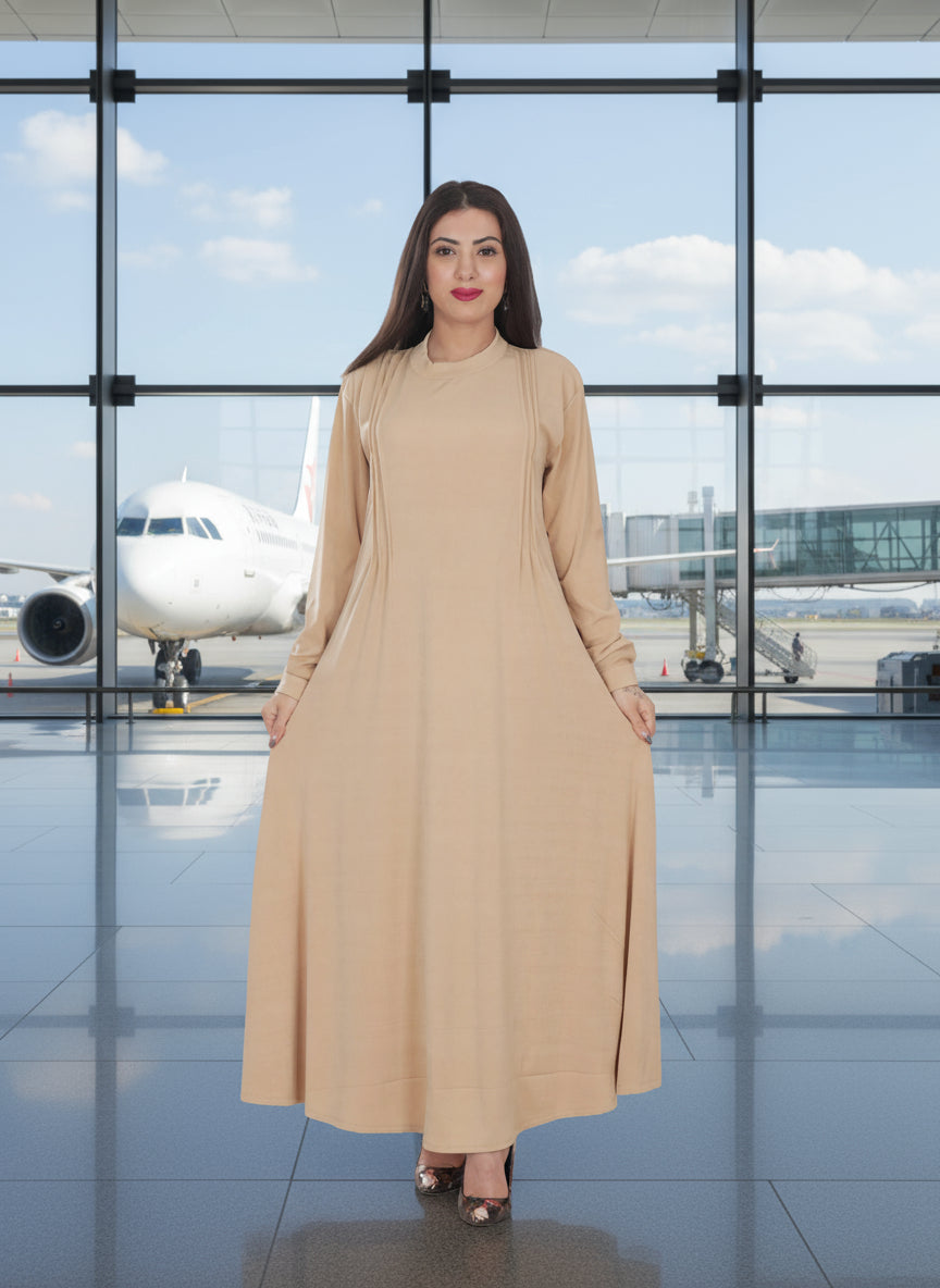 Woman in a beige dress standing in an airport terminal with an airplane visible through large windows.