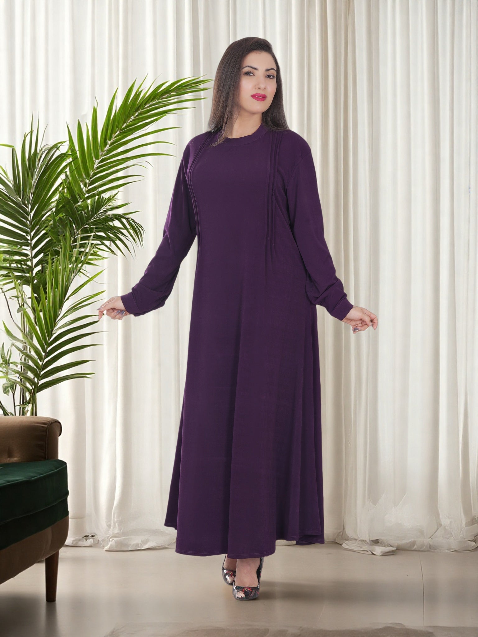 Woman wearing a purple dress standing in a room with white curtains and a plant.