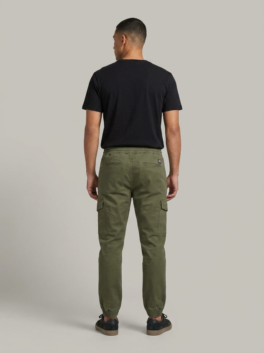 Man wearing green cargo pants and a black t-shirt on a plain background