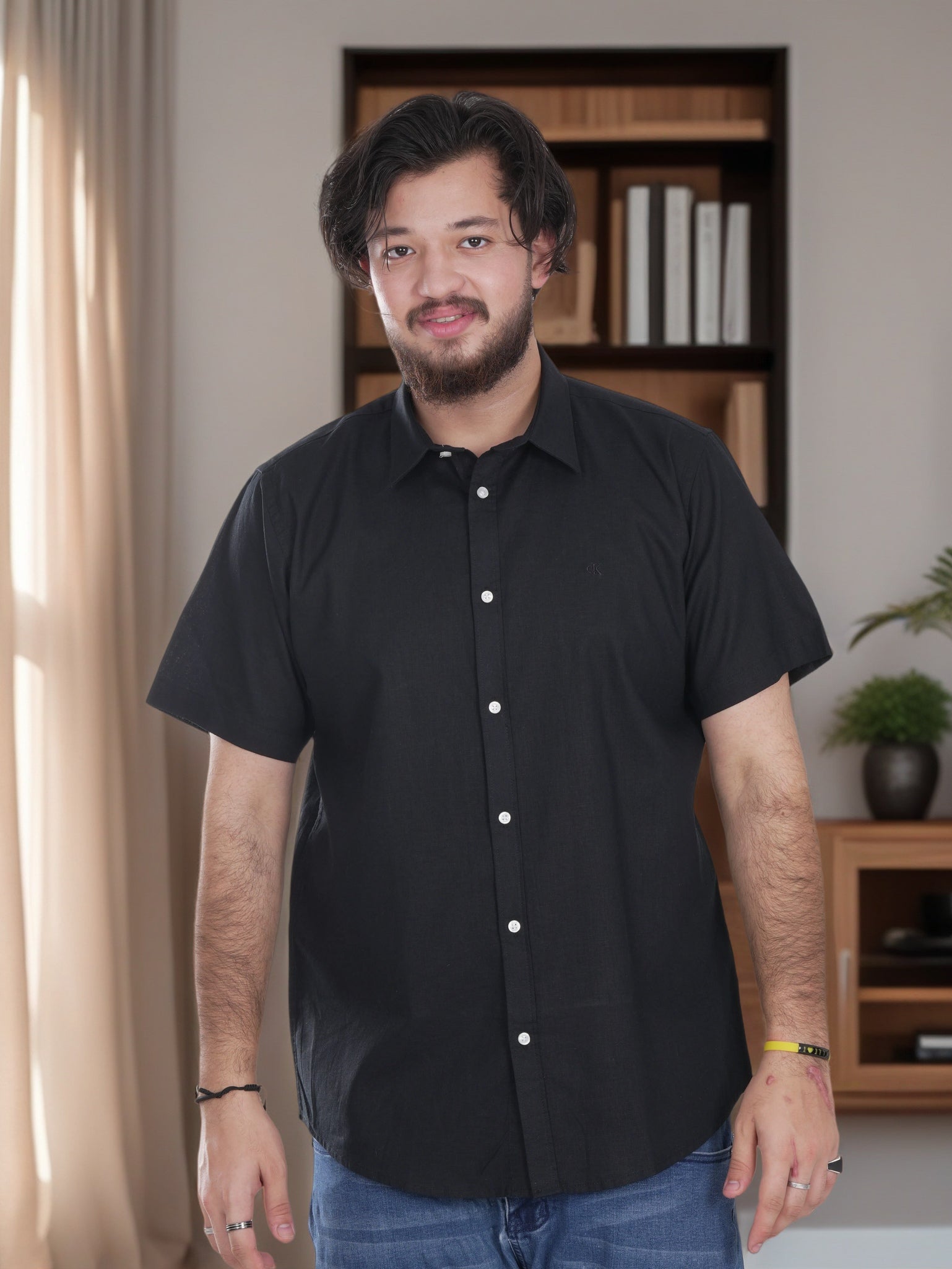 Man wearing a black shirt standing in a room with a bookshelf in the background
