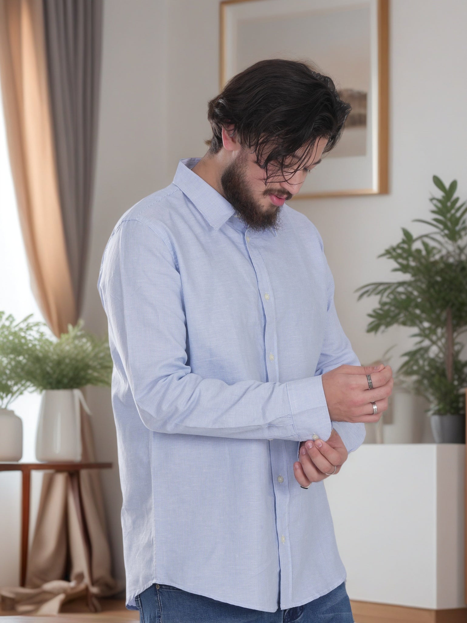 Man wearing a light blue shirt in a room with plants and a framed picture on the wall.