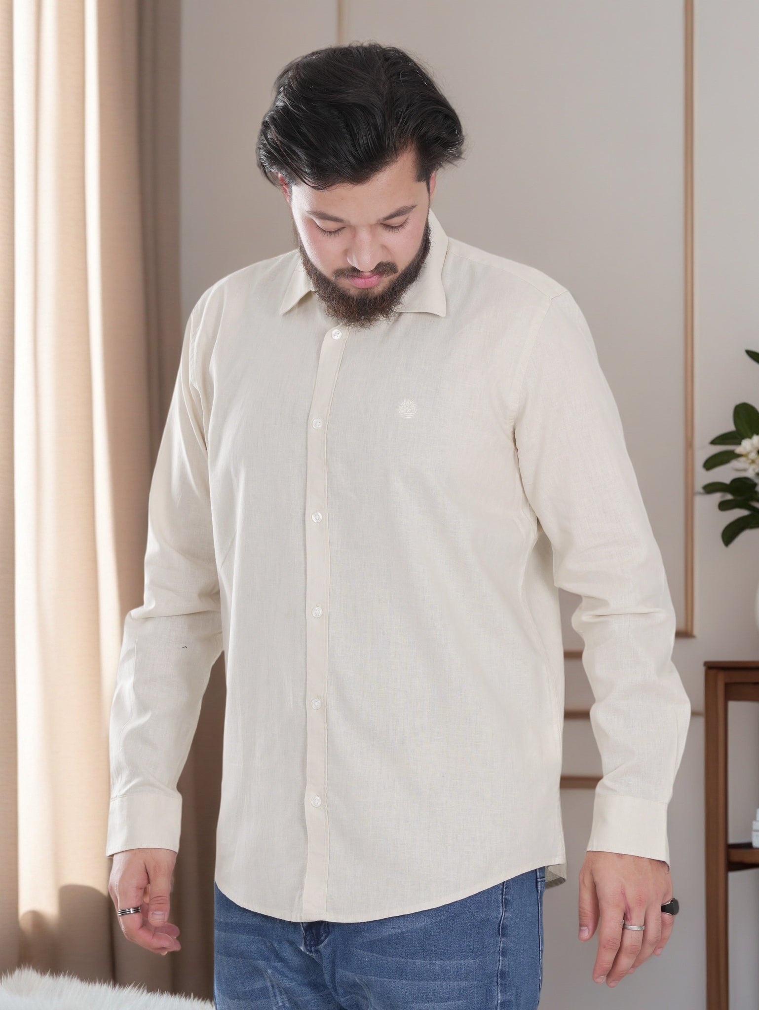 Man wearing a light-colored shirt and blue jeans indoors.