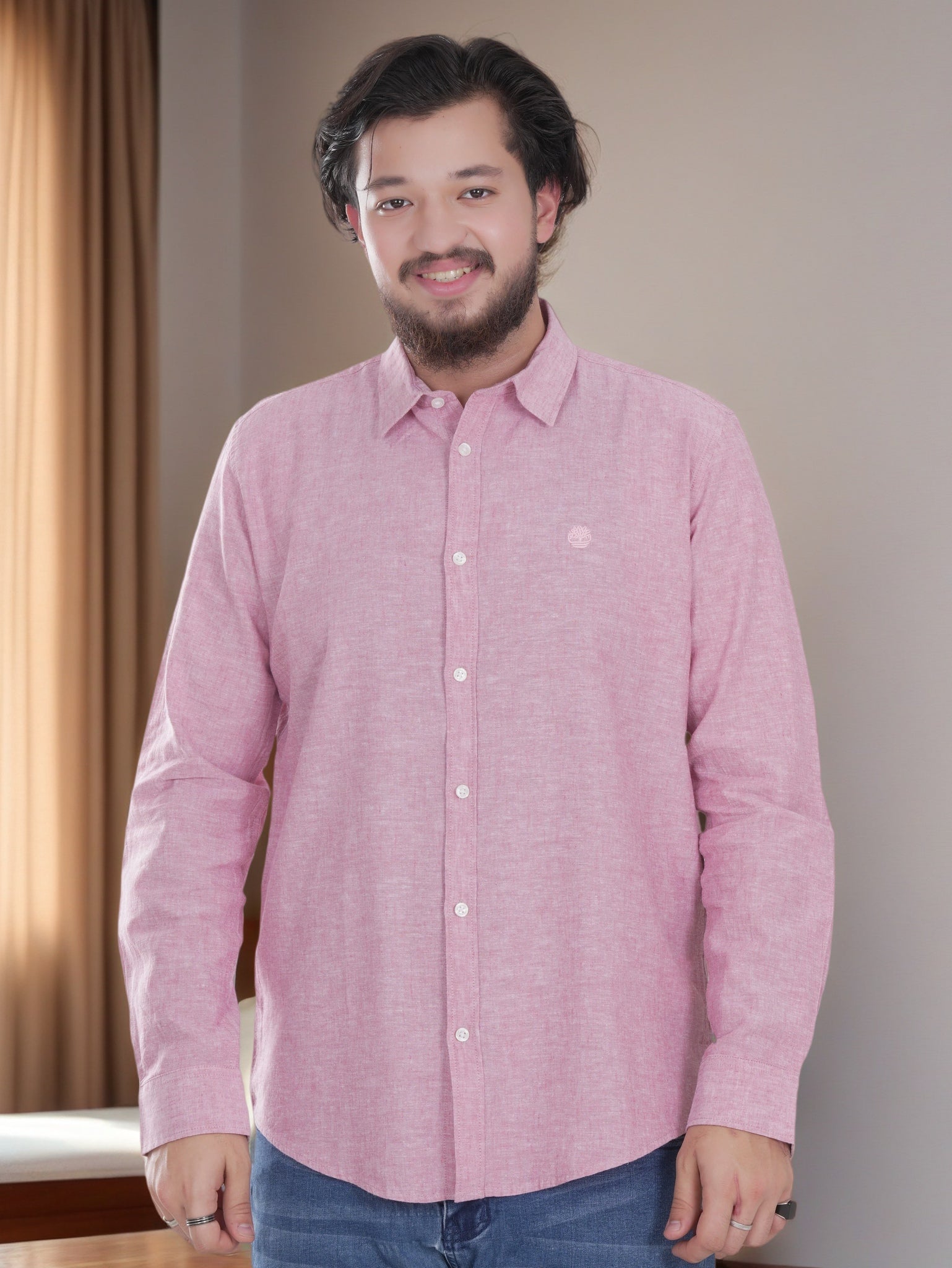 Man wearing a pink shirt standing indoors with a neutral background