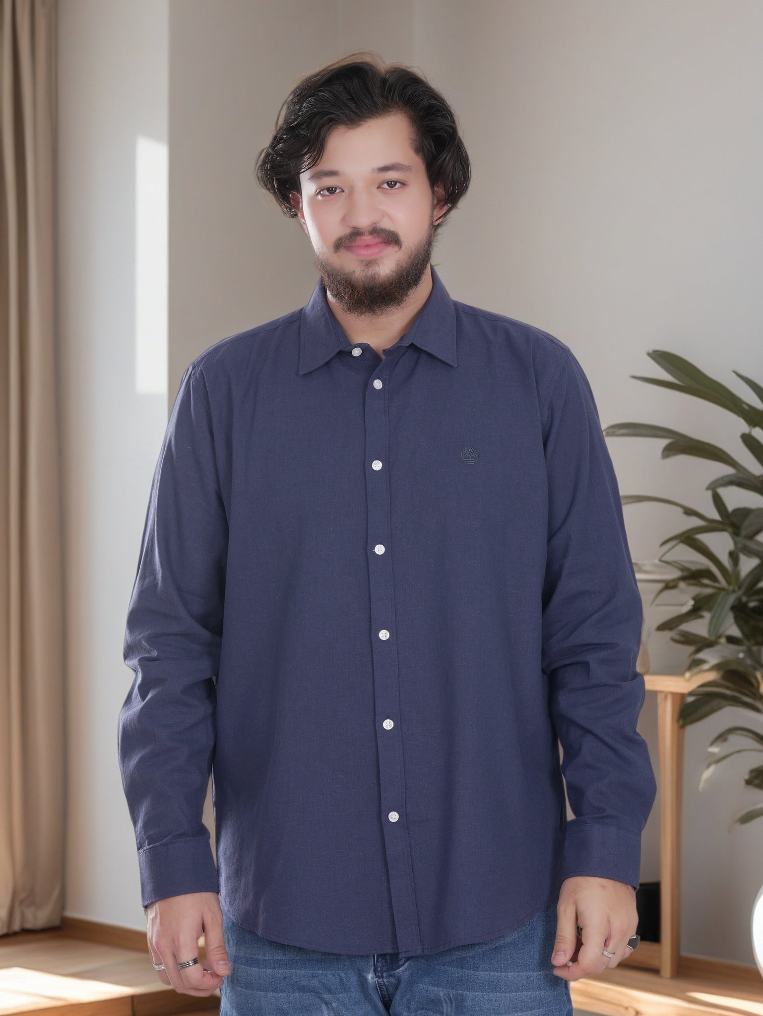 Man wearing a navy blue shirt standing indoors with a neutral background