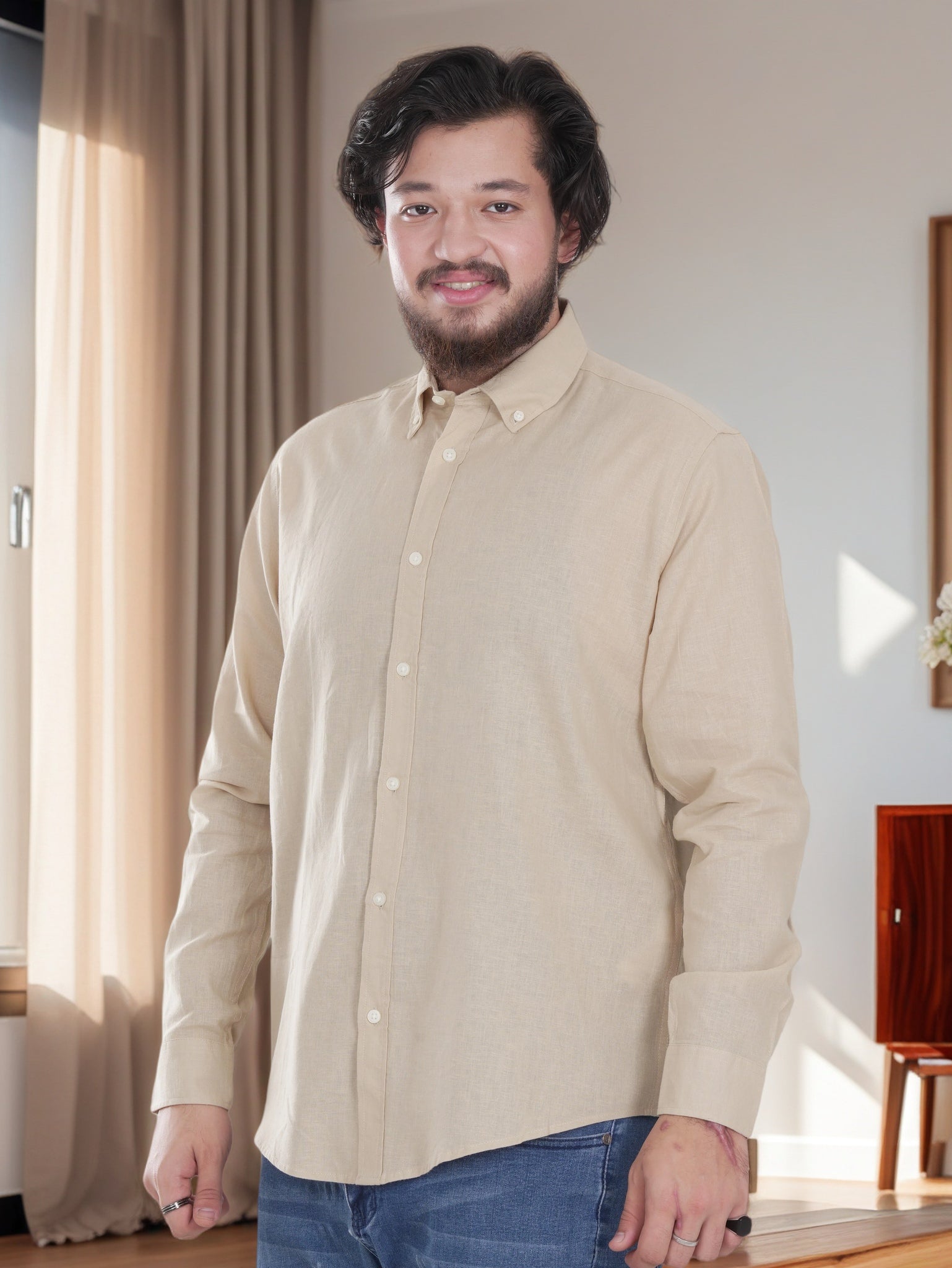 Man wearing a beige button-up shirt and blue jeans standing indoors.