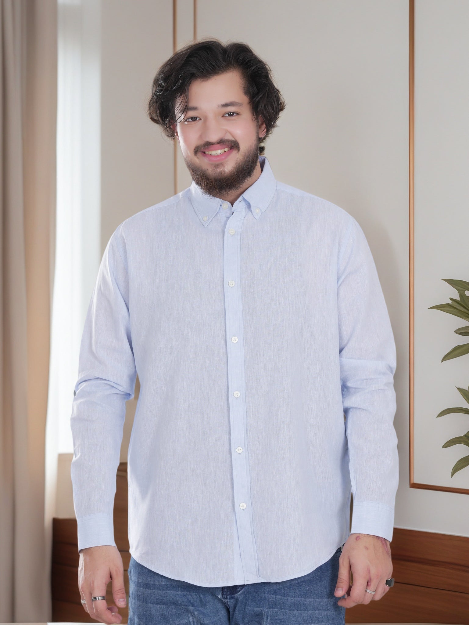 Man wearing a light blue striped shirt standing indoors with a neutral background