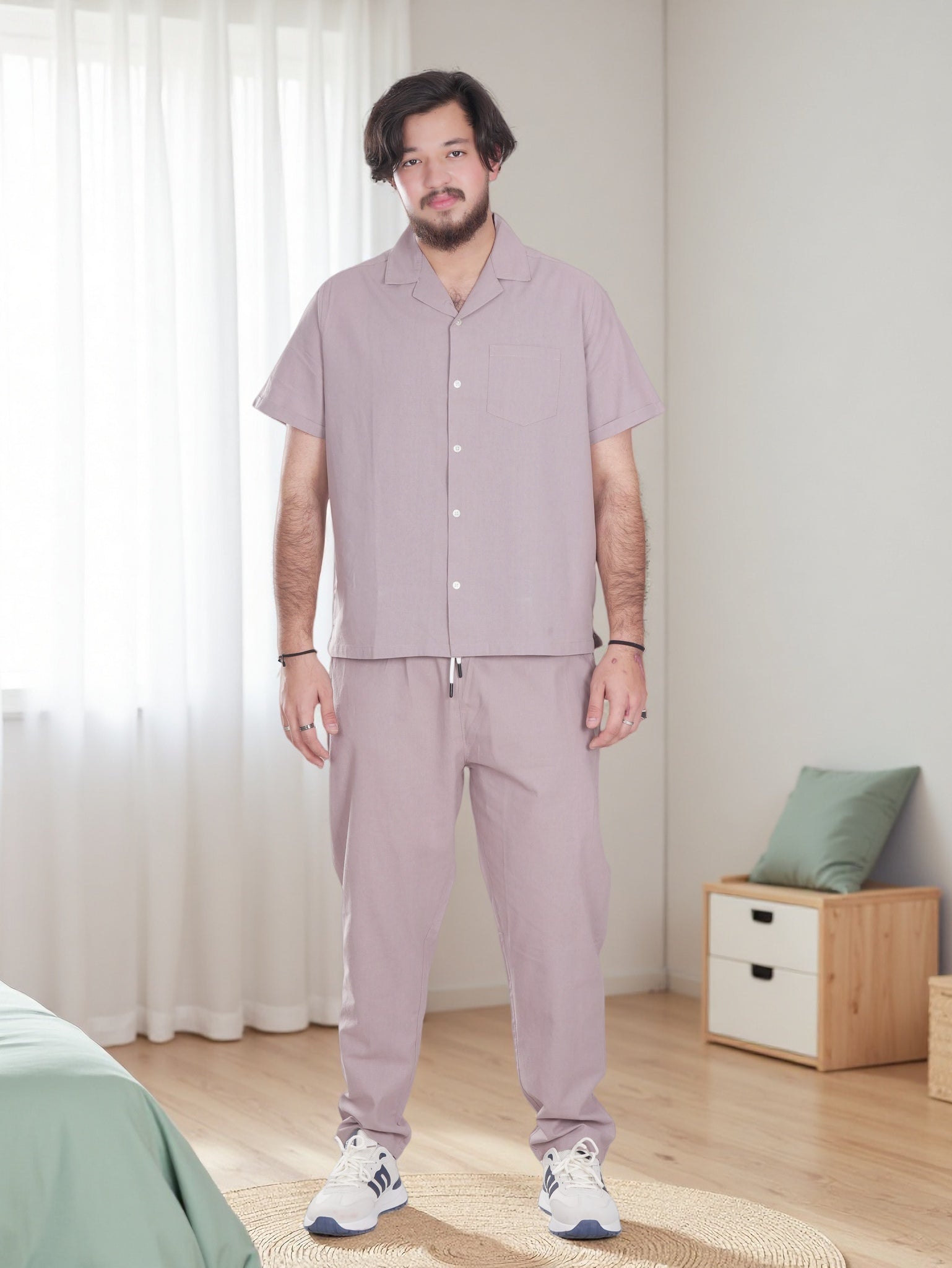 Man wearing a light purple pajama set standing in a bedroom.