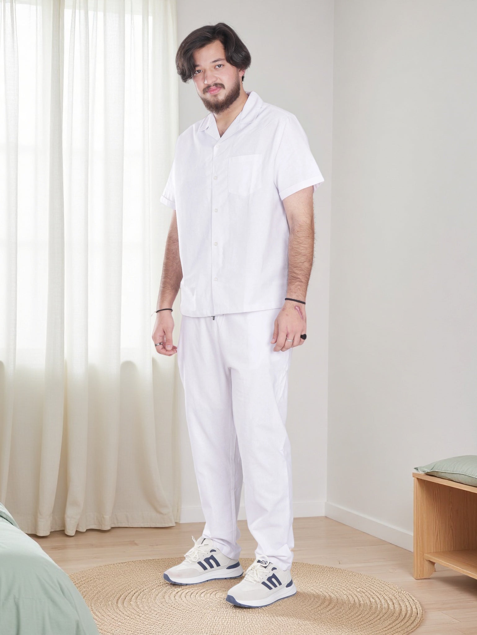 Person wearing a white outfit standing in a room with light-colored curtains and wooden floor.