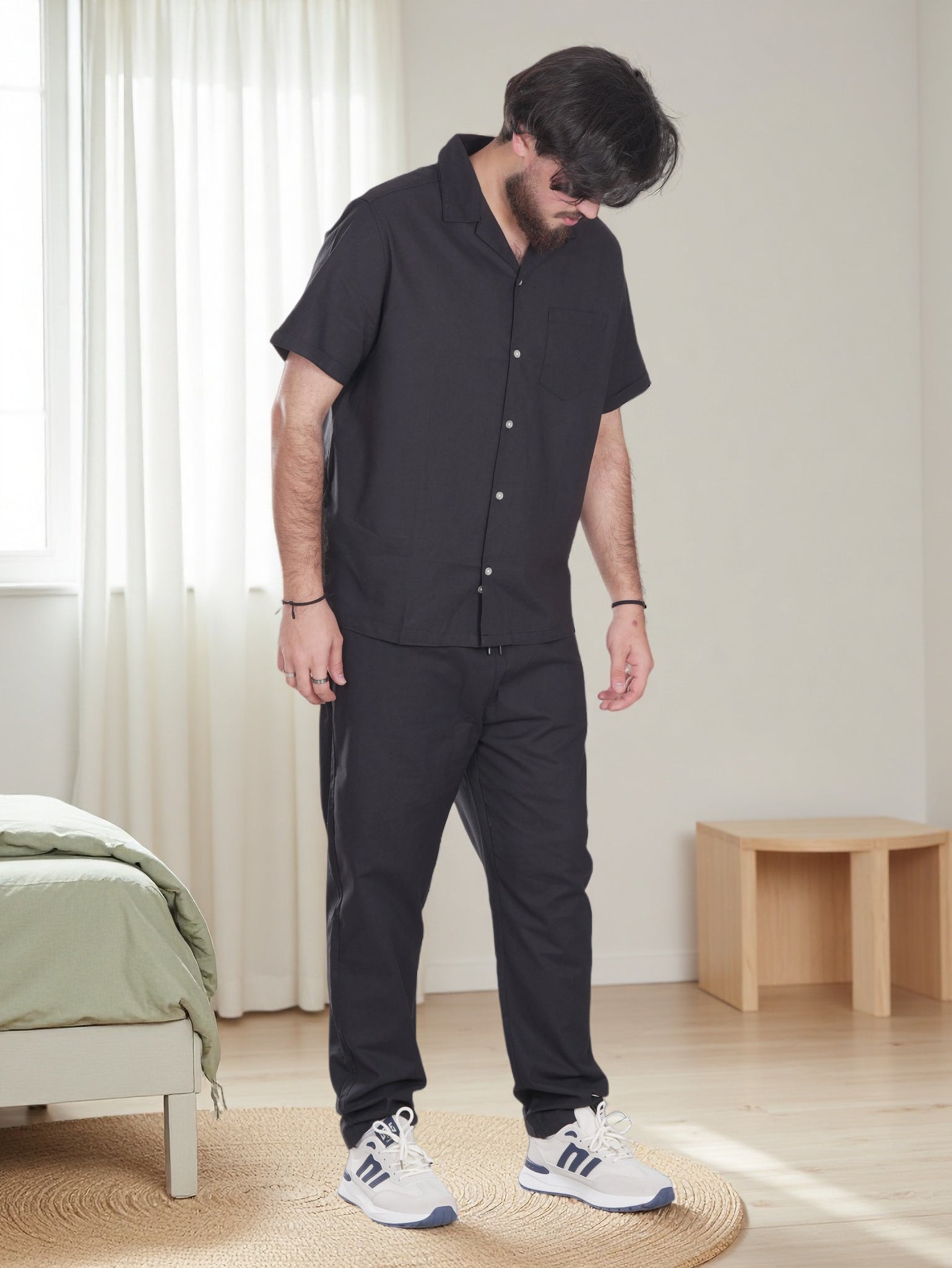 Person wearing a black outfit in a minimalistic room with a bed and table.