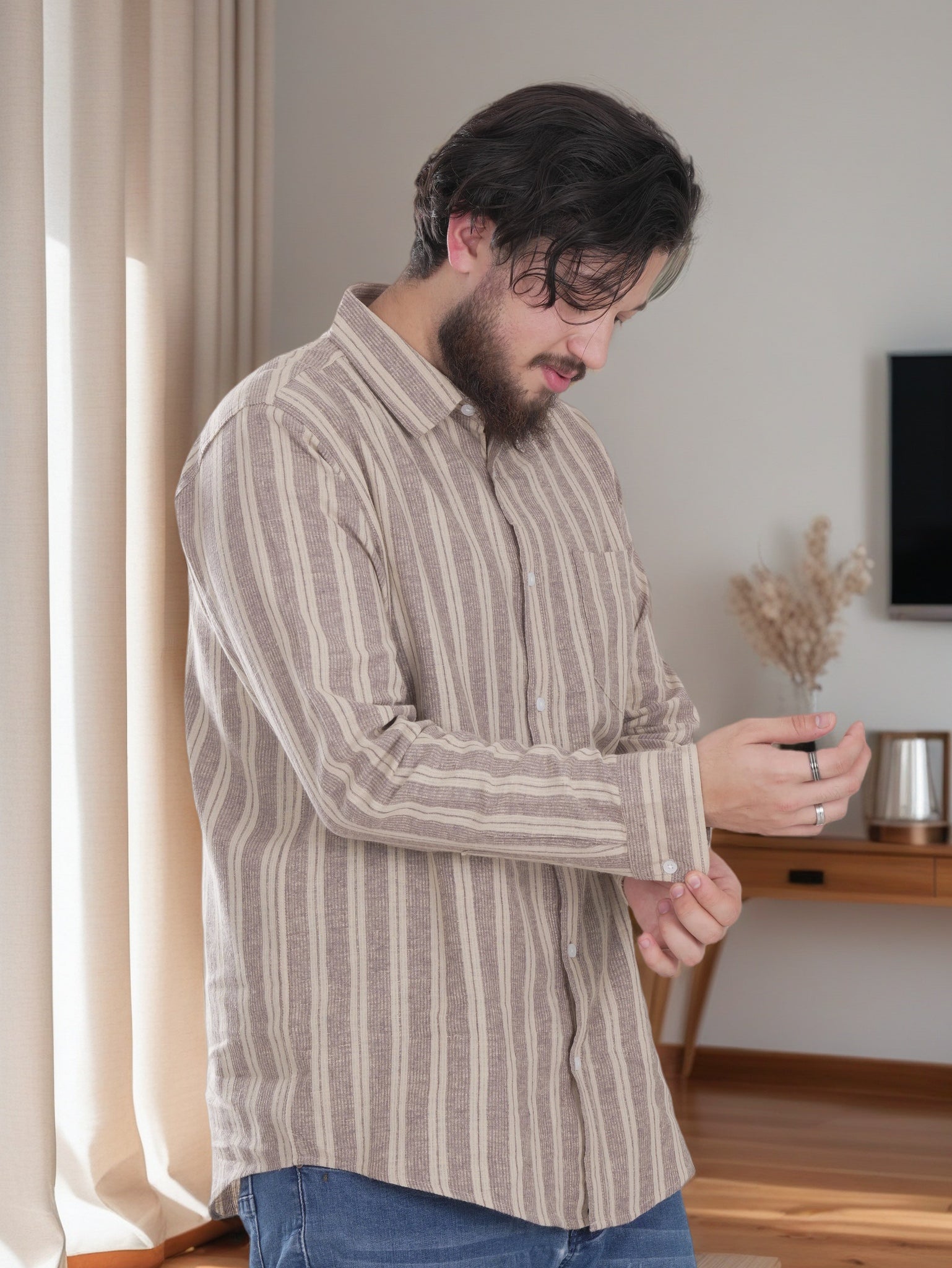 Man wearing a striped shirt in a room with a curtain and TV in the background