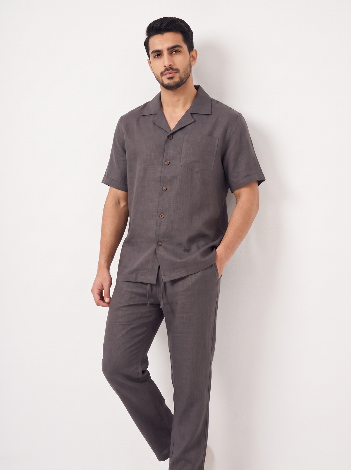 A man modeling a dark gray short-sleeve button-up pajama shirt and matching trousers against a plain white studio background.