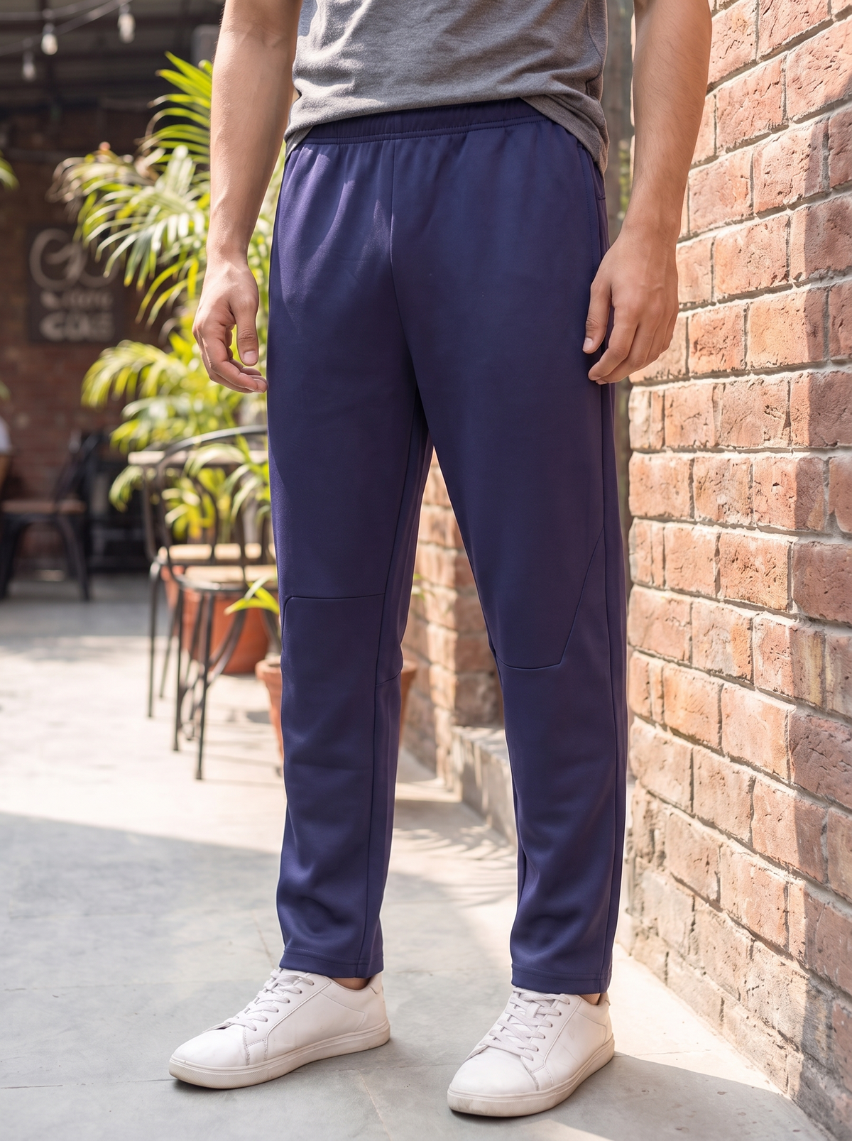 A person wearing navy blue athletic jogger pants with side pockets, paired with a gray t-shirt and white sneakers, standing outdoors next to a brick wall.