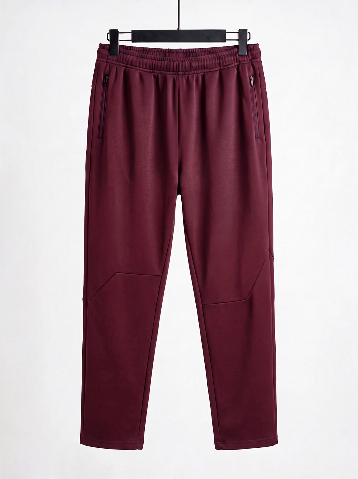 A pair of dark burgundy jogger-style pants with zippered side pockets and a drawstring waist, hanging on a black hanger against a plain white background.