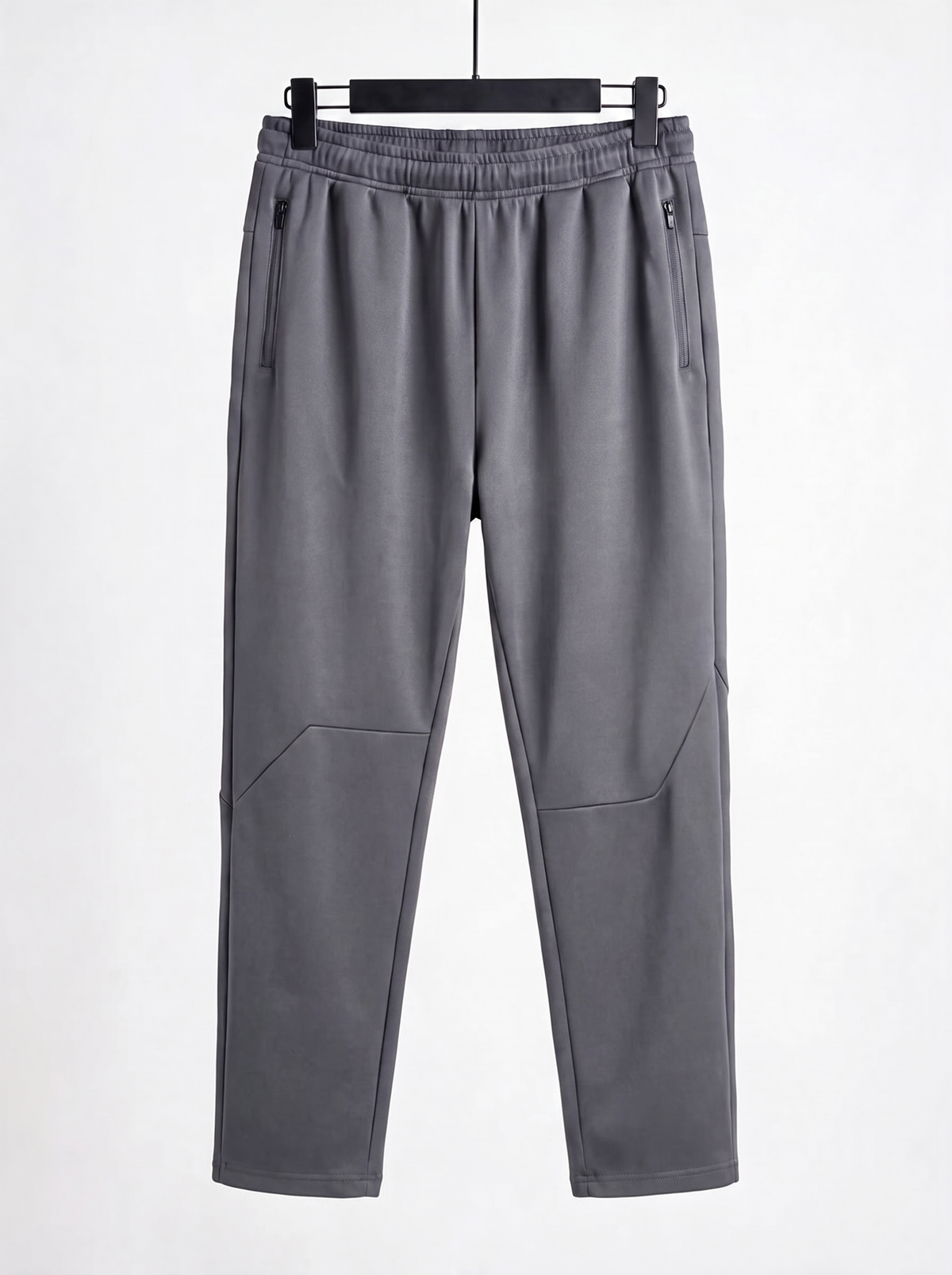 A pair of gray athletic pants hanging on a black hanger against a plain white background. The pants feature an elastic waistband, zippered side pockets, and angled seam details on the lower legs.