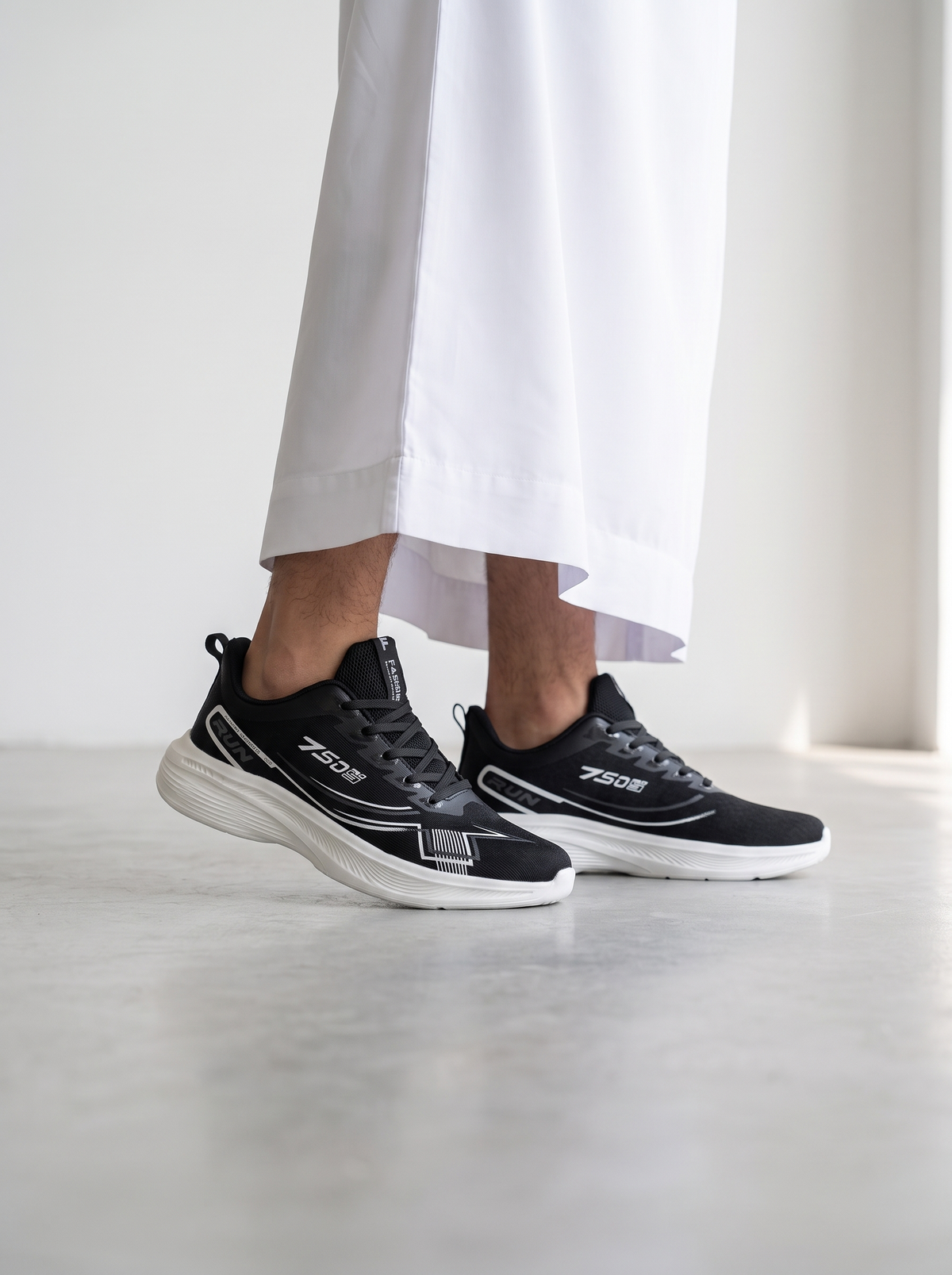 A person wearing black and white ZEON sneakers with white wide-leg trousers, standing on a light gray concrete floor against a white wall.