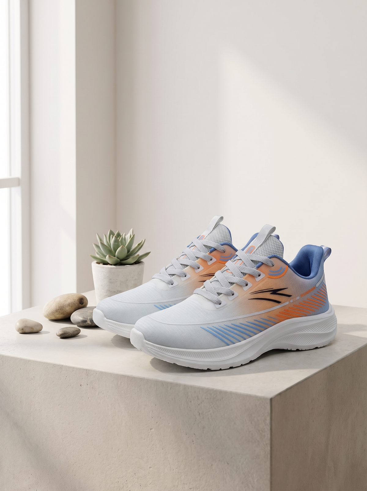 A pair of athletic sneakers in white with orange and blue accents, displayed on a light concrete block next to a small potted succulent with decorative stones.