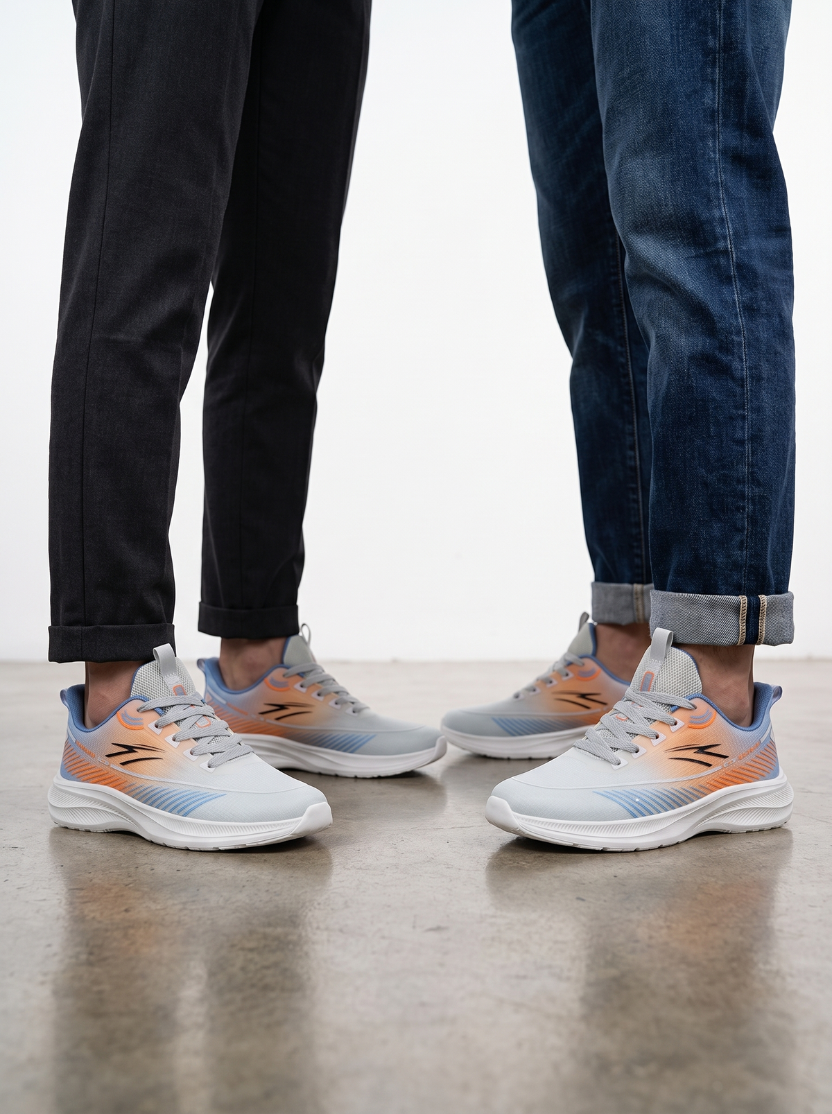 A pair of athletic sneakers shown on two models' feet, with one person wearing black pants and the other wearing blue jeans. The sneakers feature a light gray and white upper with a peach-to-orange gradient and light blue accents.