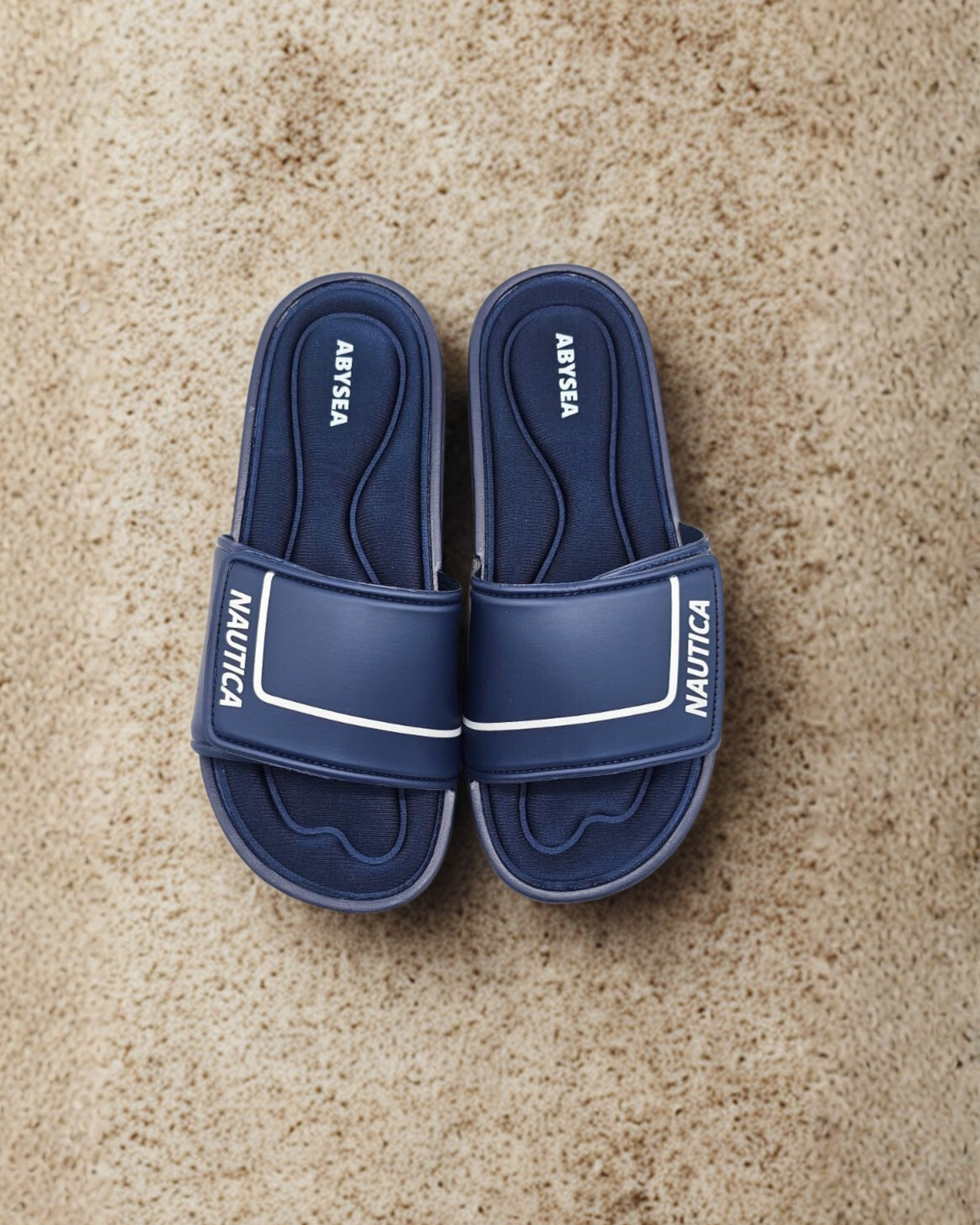 Pair of blue Nautica slides on a beige carpet