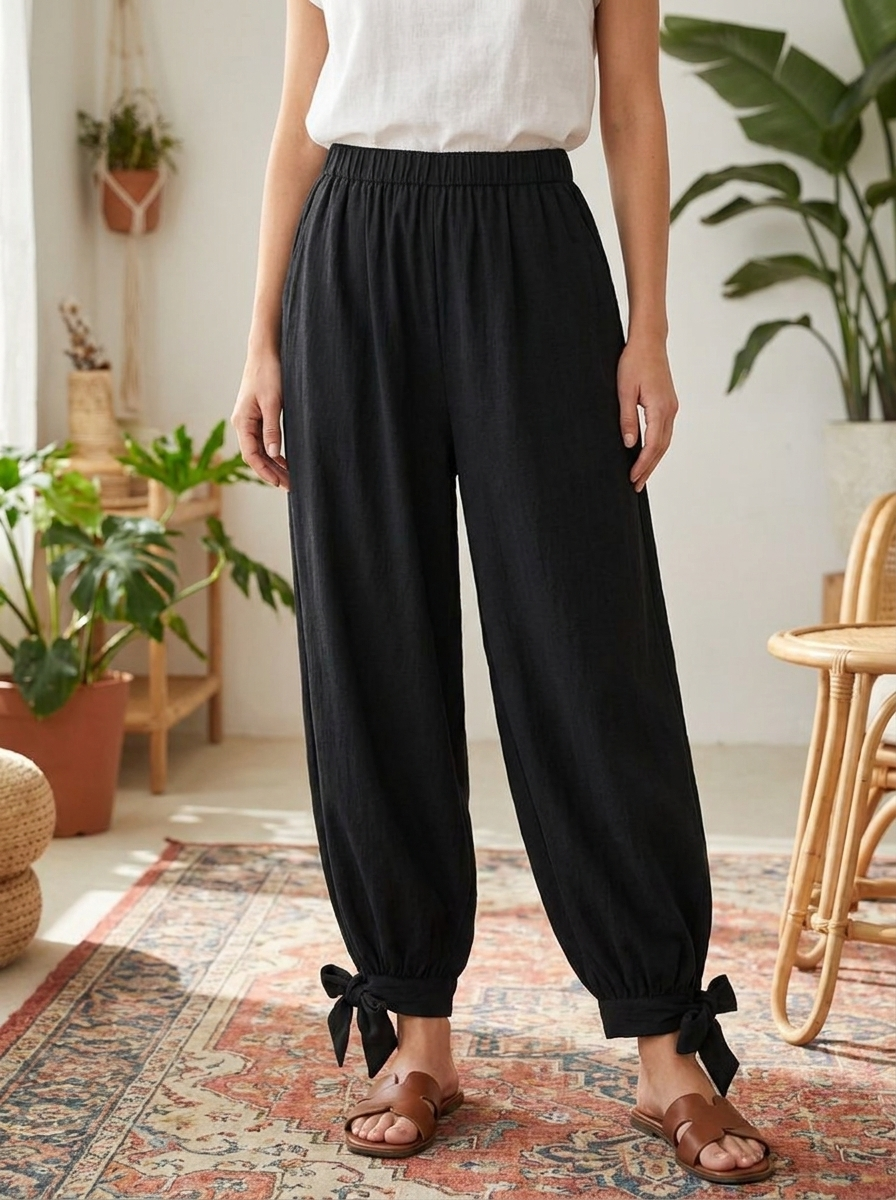 Person wearing black pants with tied ankles in a home setting with plants and furniture.