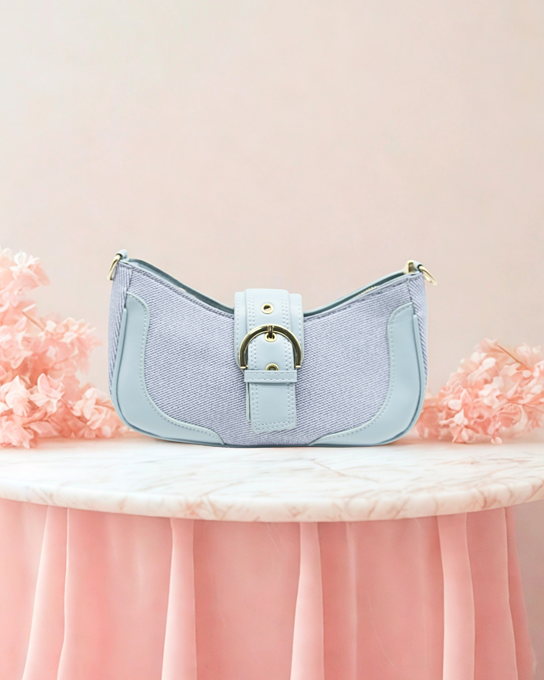 Light blue handbag with a gold buckle on a pink floral and marble surface