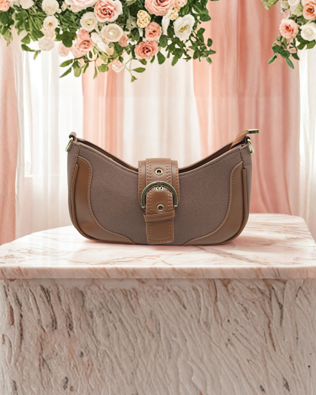 Brown leather handbag with decorative buckle on a marble surface with floral decorations.