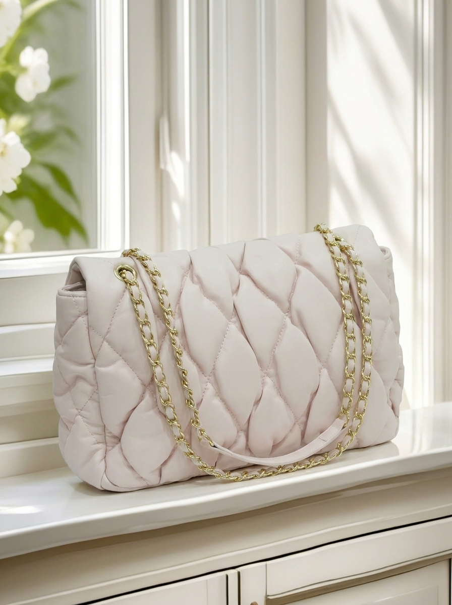 Quilted handbag with gold chain strap on a surface near a window with white curtains.