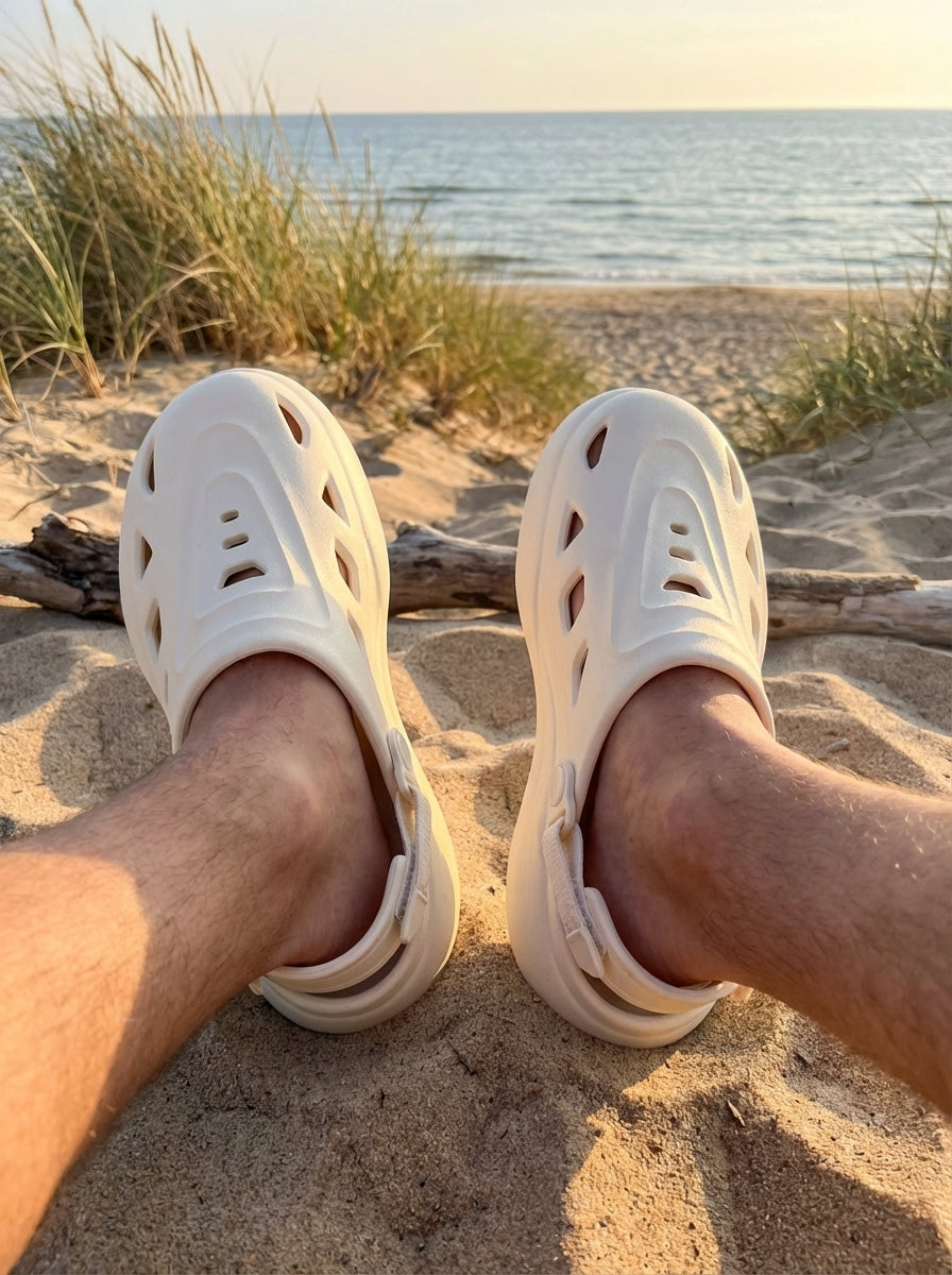 White sandals on a sandy beach with grass and water in the background