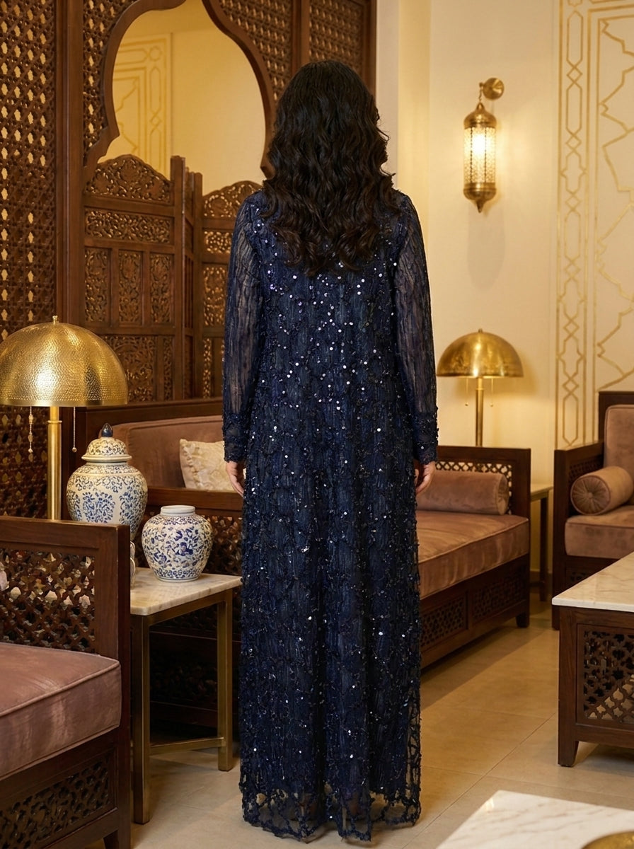 Woman in a dark blue sequined dress standing in a decorated room with wooden furniture and decorative elements.