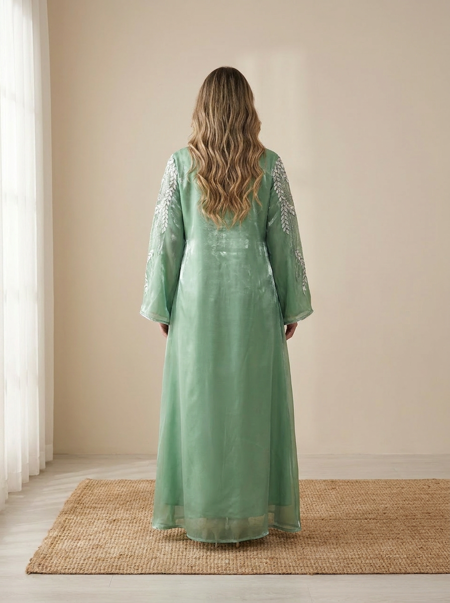 Woman wearing a green dress with intricate patterns in a minimalistic room.