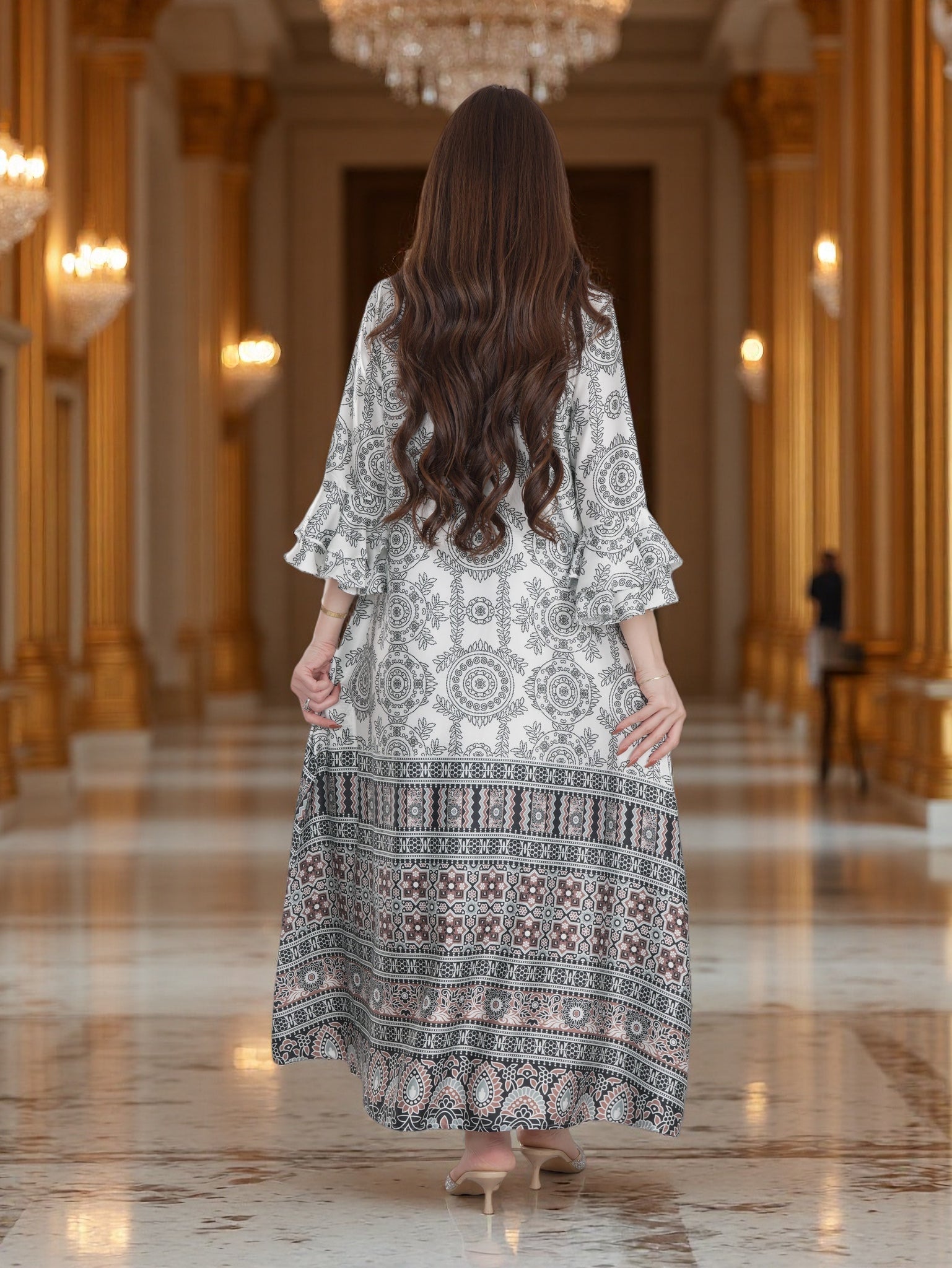 Woman in a long, patterned dress standing in an elegant hallway with chandeliers.