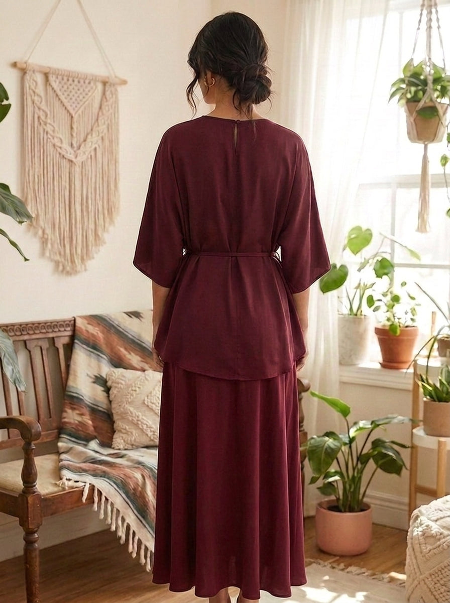 Woman in a burgundy dress standing in a room with plants and decor.