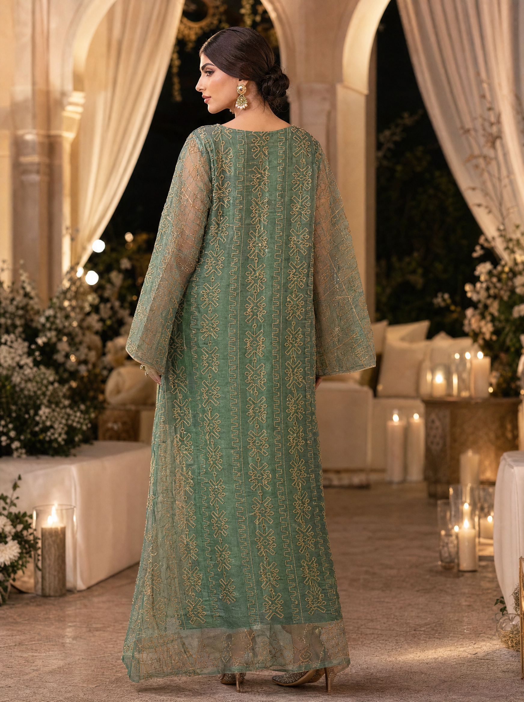 Woman in a green embroidered dress standing in an elegant indoor setting with floral decorations and candles.