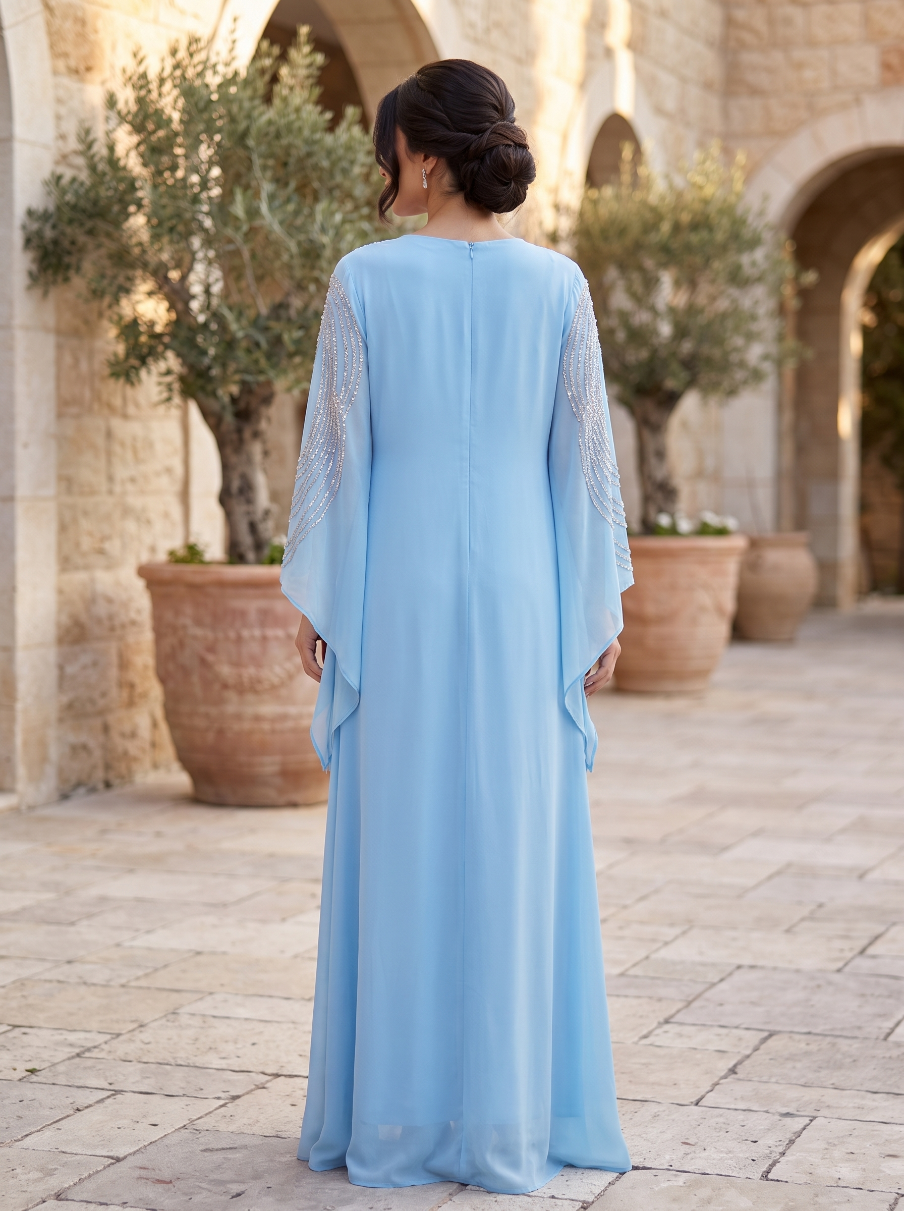 Woman in a light blue dress standing in an outdoor setting with stone arches and potted plants.