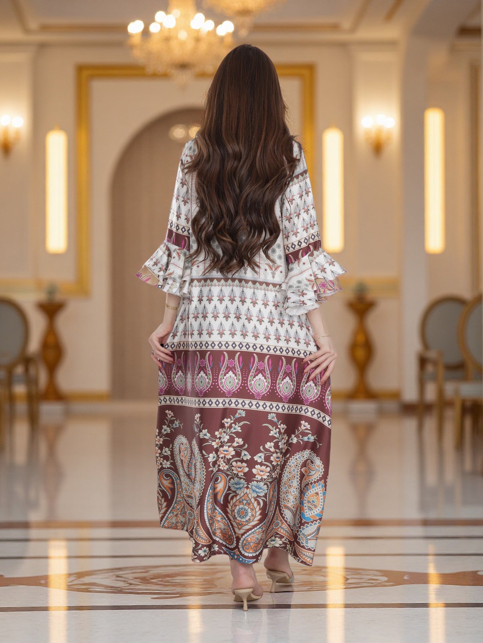 Woman in a patterned dress standing in an elegant room with chandeliers.