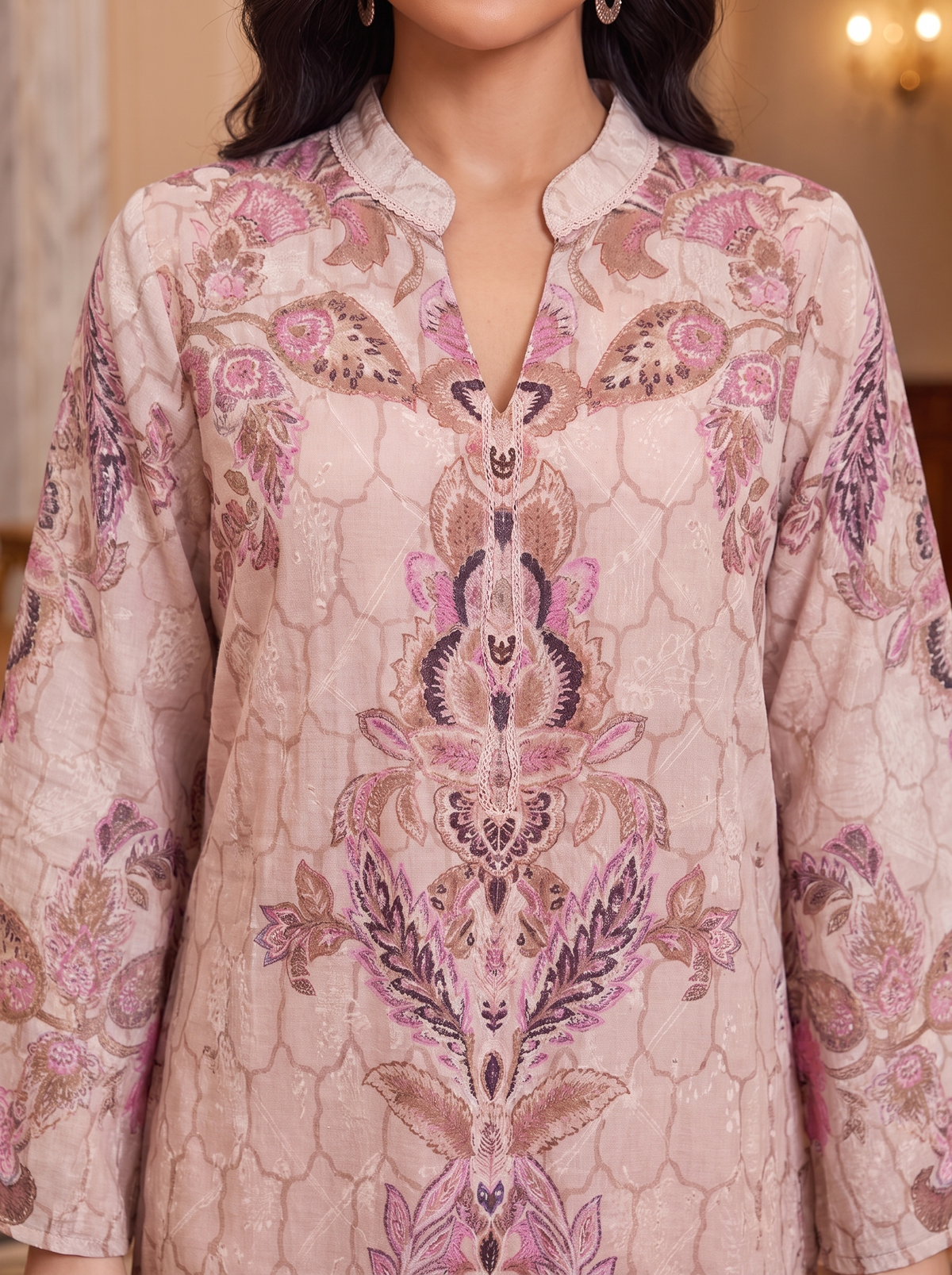 A close-up of a woman wearing a light pink embroidered kurta with intricate floral and geometric patterns in pink, purple, and brown.