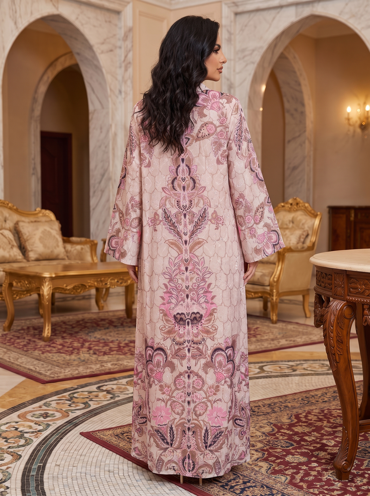 A woman stands in a grand, ornate room wearing a long, flowing kaftan-style dress with a pink and beige floral pattern, photographed from behind.