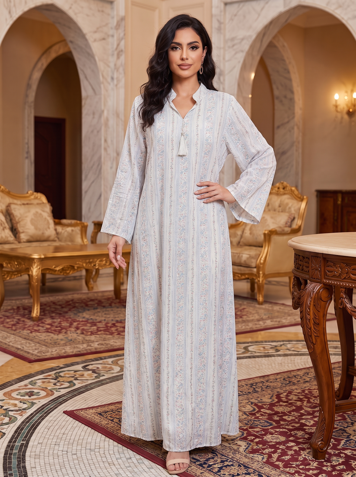 A woman modeling a long, light blue and white patterned kaftan dress in an ornate, traditional Middle Eastern interior with marble arches and gold furniture.