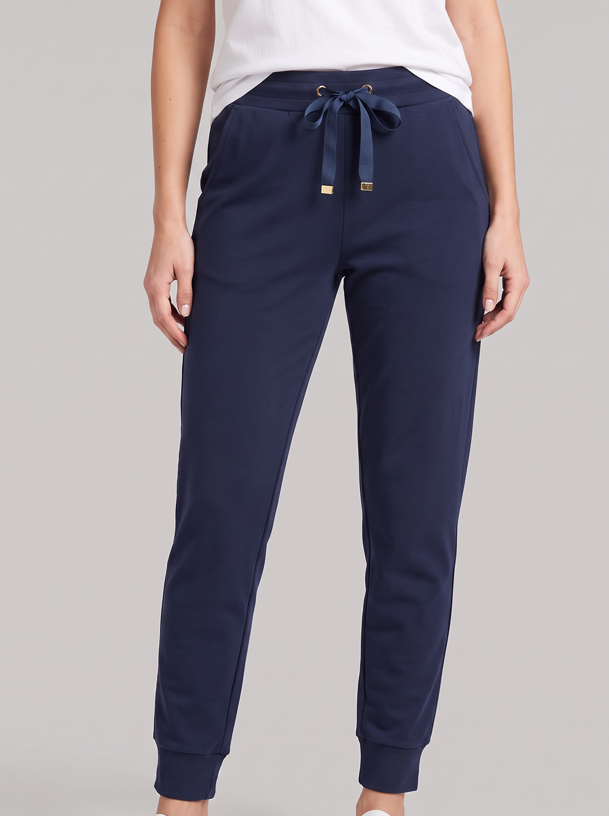 A person wearing navy jogger-style pants with a drawstring waist and ribbed cuffs, paired with a white top, against a light gray studio background.