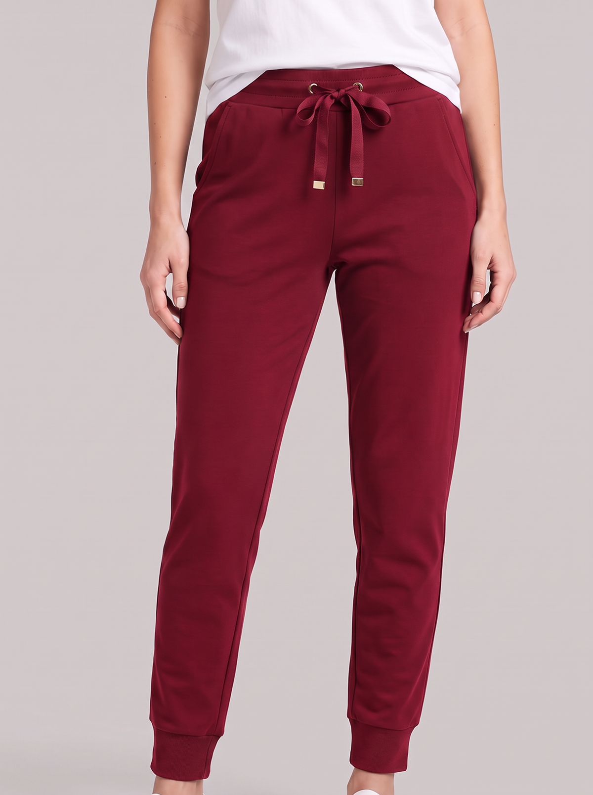 A person wearing jogger-style pants in deep burgundy, paired with a white top, shown from the waist down against a plain light gray studio background.