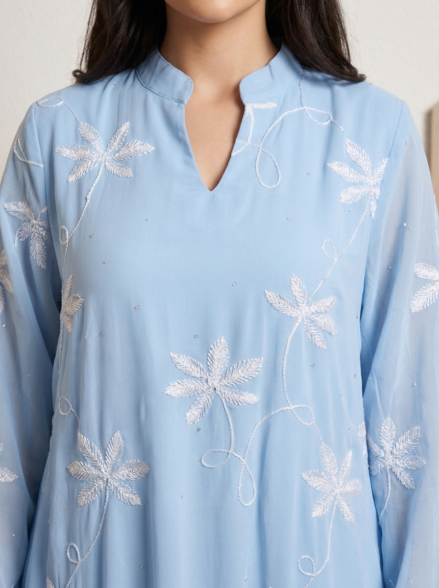 A close-up of a light blue long-sleeve tunic or kurta with white floral embroidery and a split neckline, worn by a model.