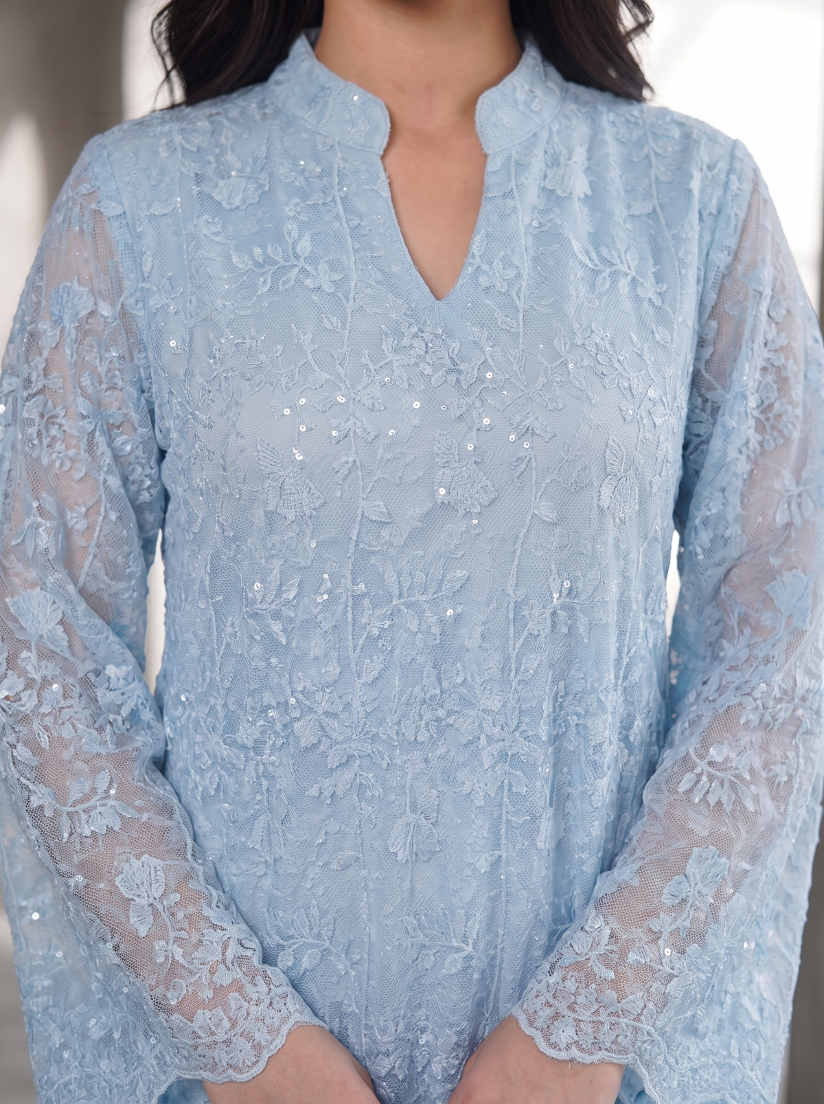 A light blue lace long-sleeve tunic top with a split neckline and delicate sequin embellishments, shown on a model.