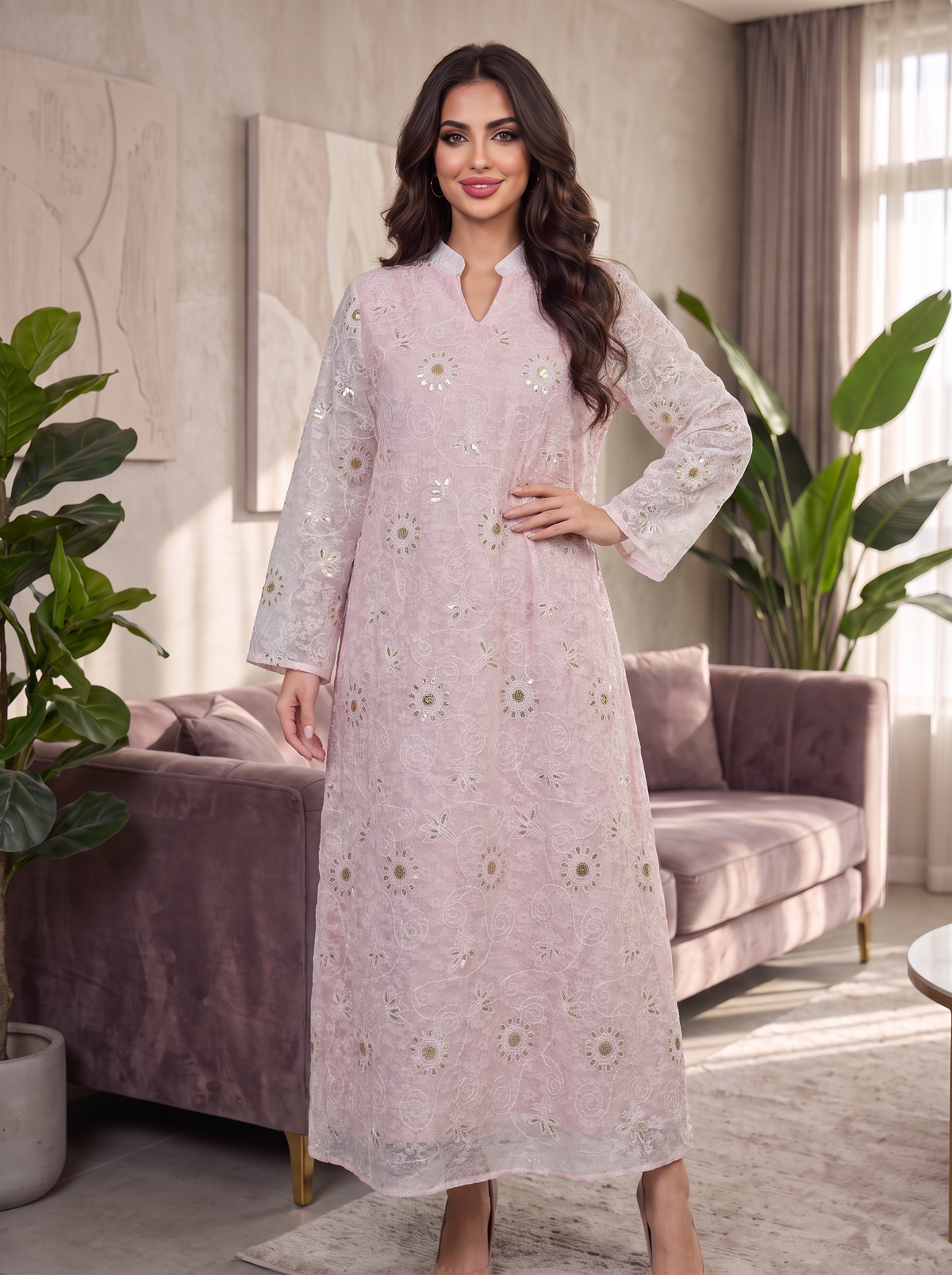 A woman modeling a light pink long kurta with white floral embroidery, standing in a modern living room setting with a purple sofa and green plants.