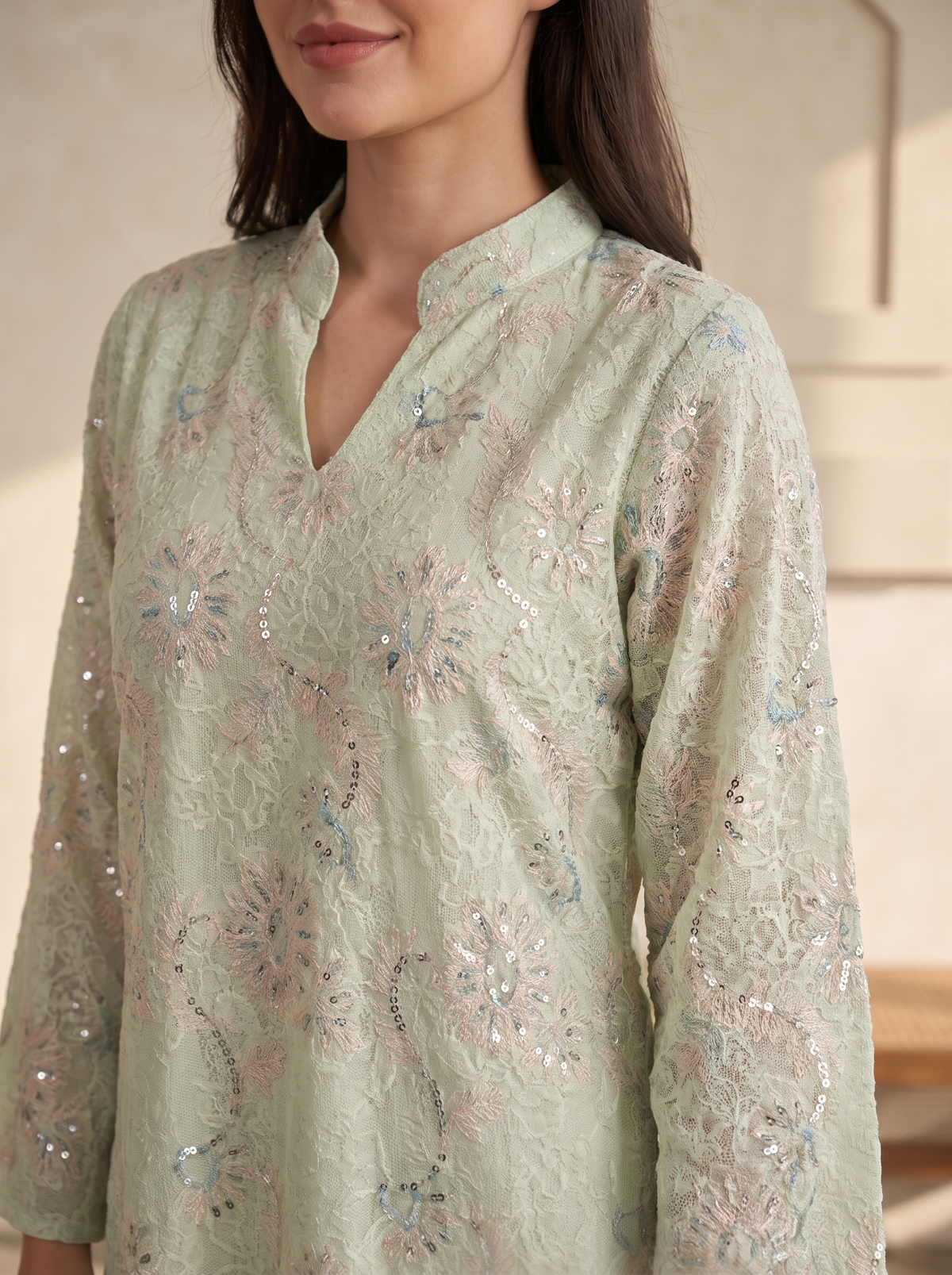A close-up of a woman wearing a light sage green embroidered kurta with floral patterns and sequins, featuring a split neckline and long sleeves.