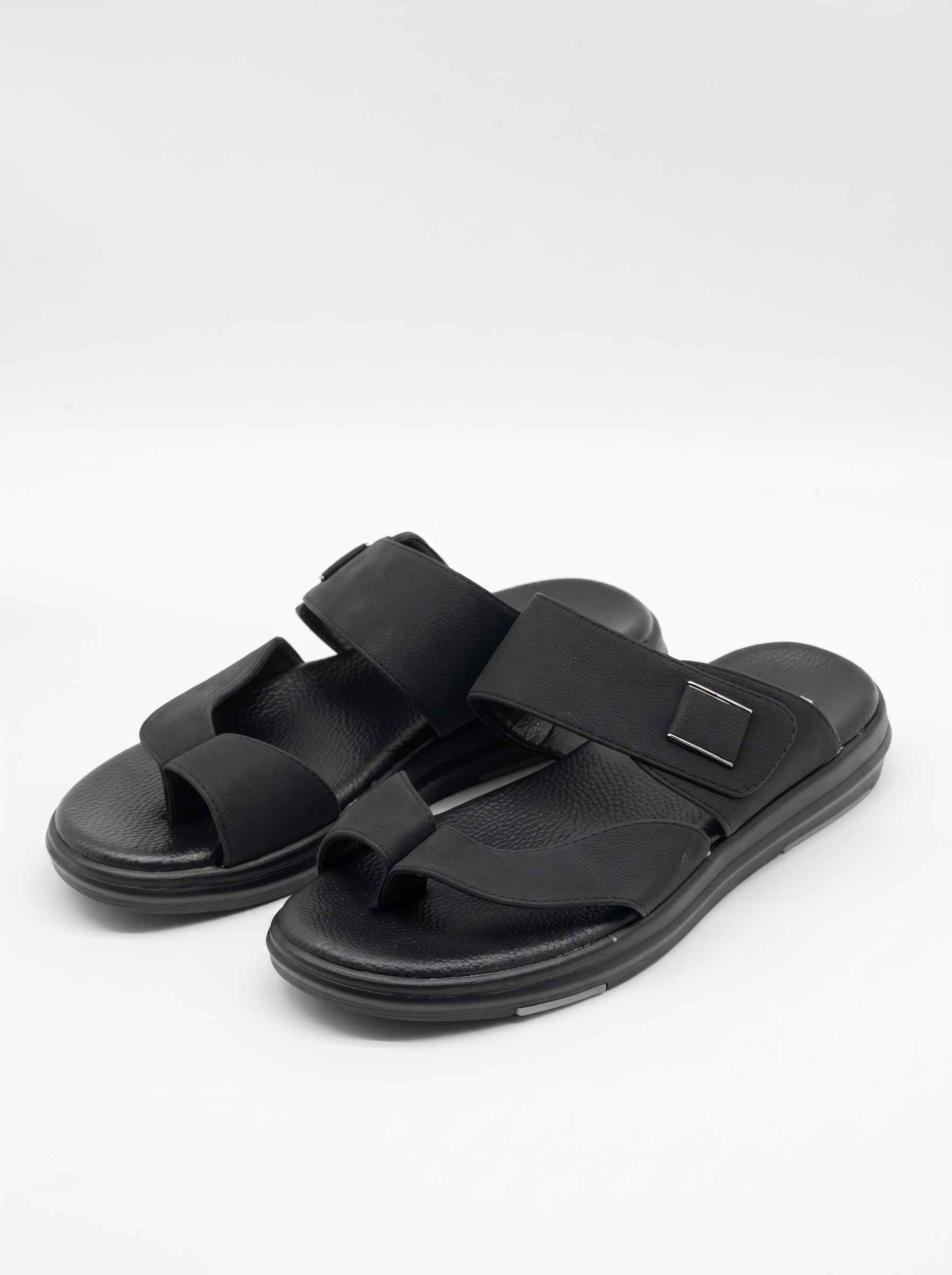 A pair of black double-strap slide sandals with adjustable hook-and-loop straps and a small square metal accent, shown on a light gray studio background.