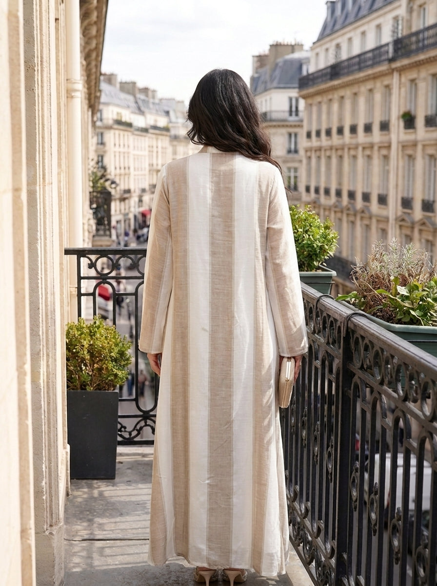 Woman in a long beige coat standing on a balcony with cityscape in the background